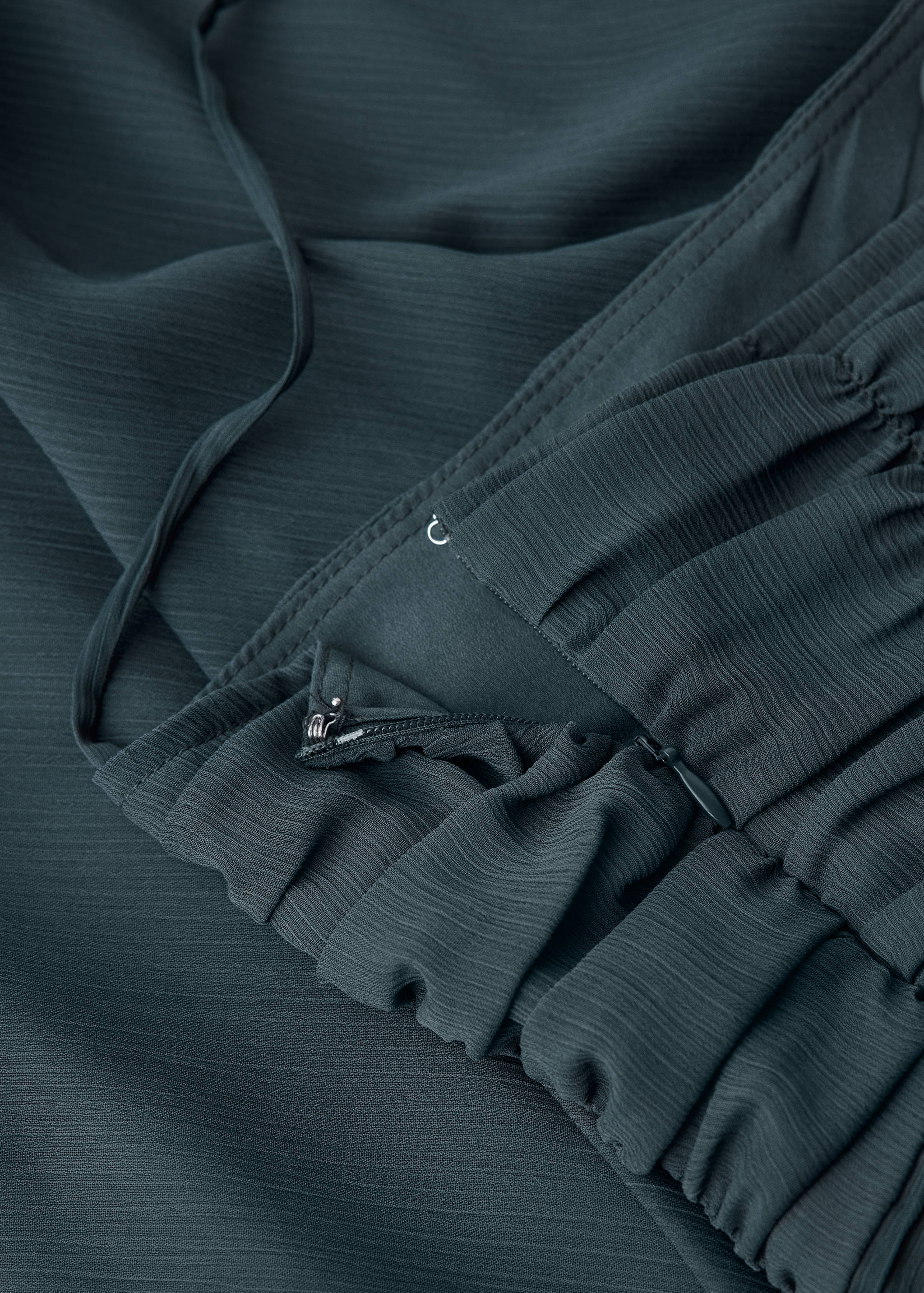 Close-up of the textured fabric and side zip fastening on a dark green dress.