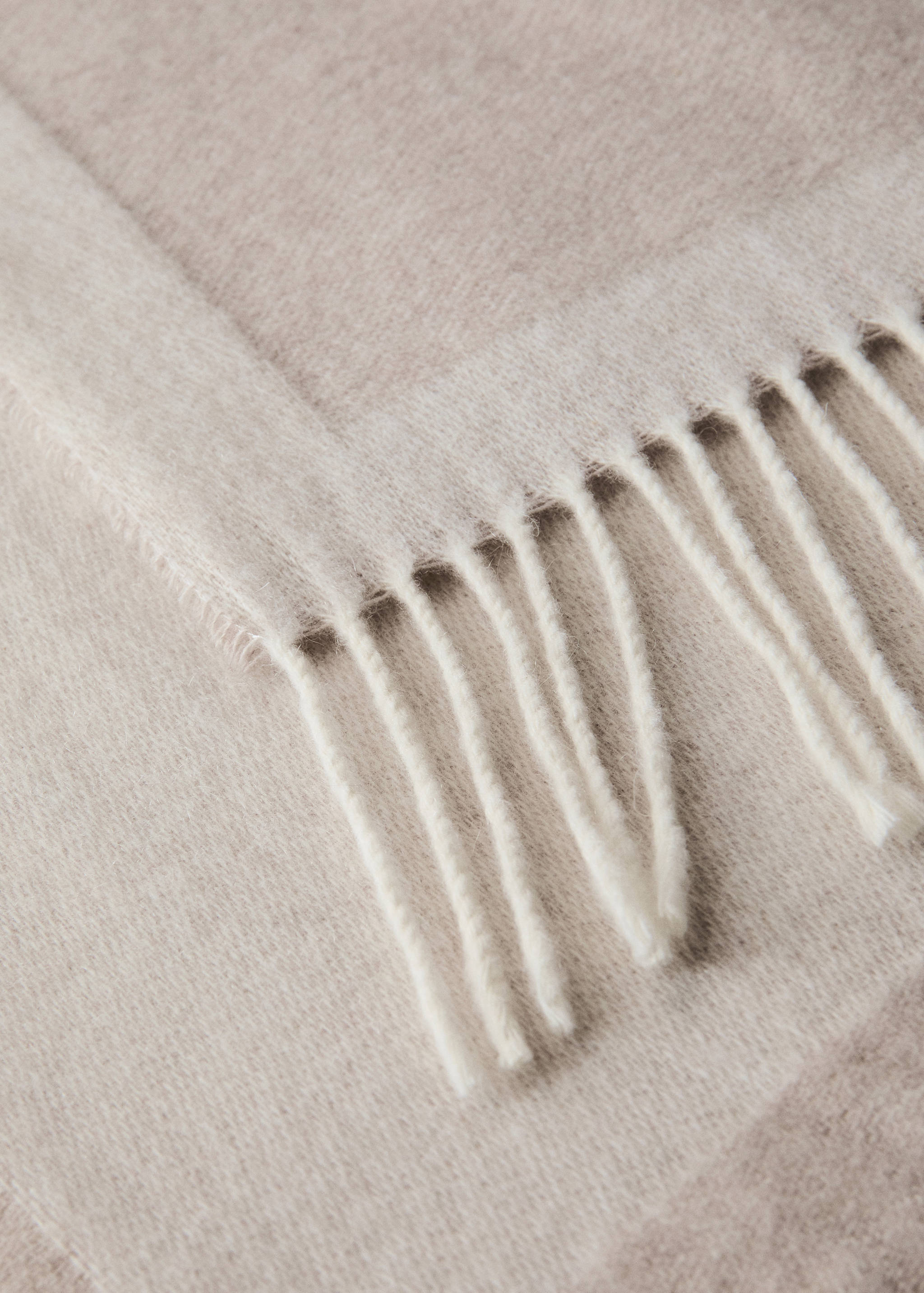 Close-up of a soft beige blanket featuring a textured weave and fringed edges.