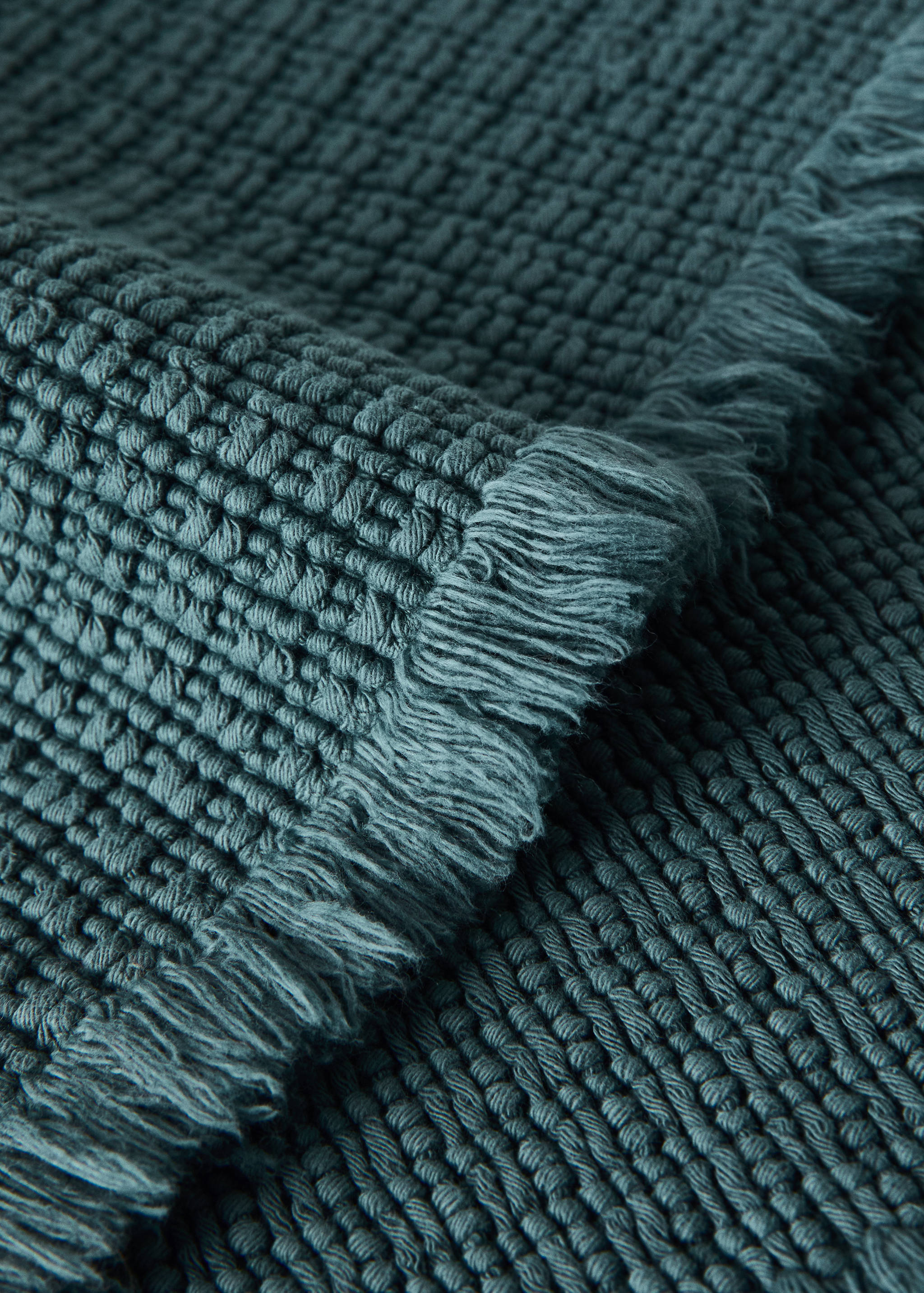 Dark teal textured bath mat with fringe detail.