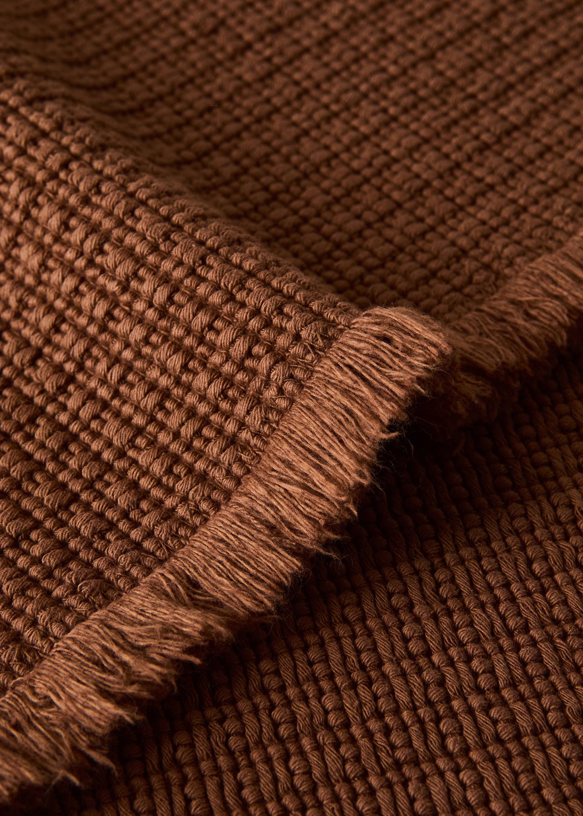 Brown waffle-weave bathroom mat with fringed edges.