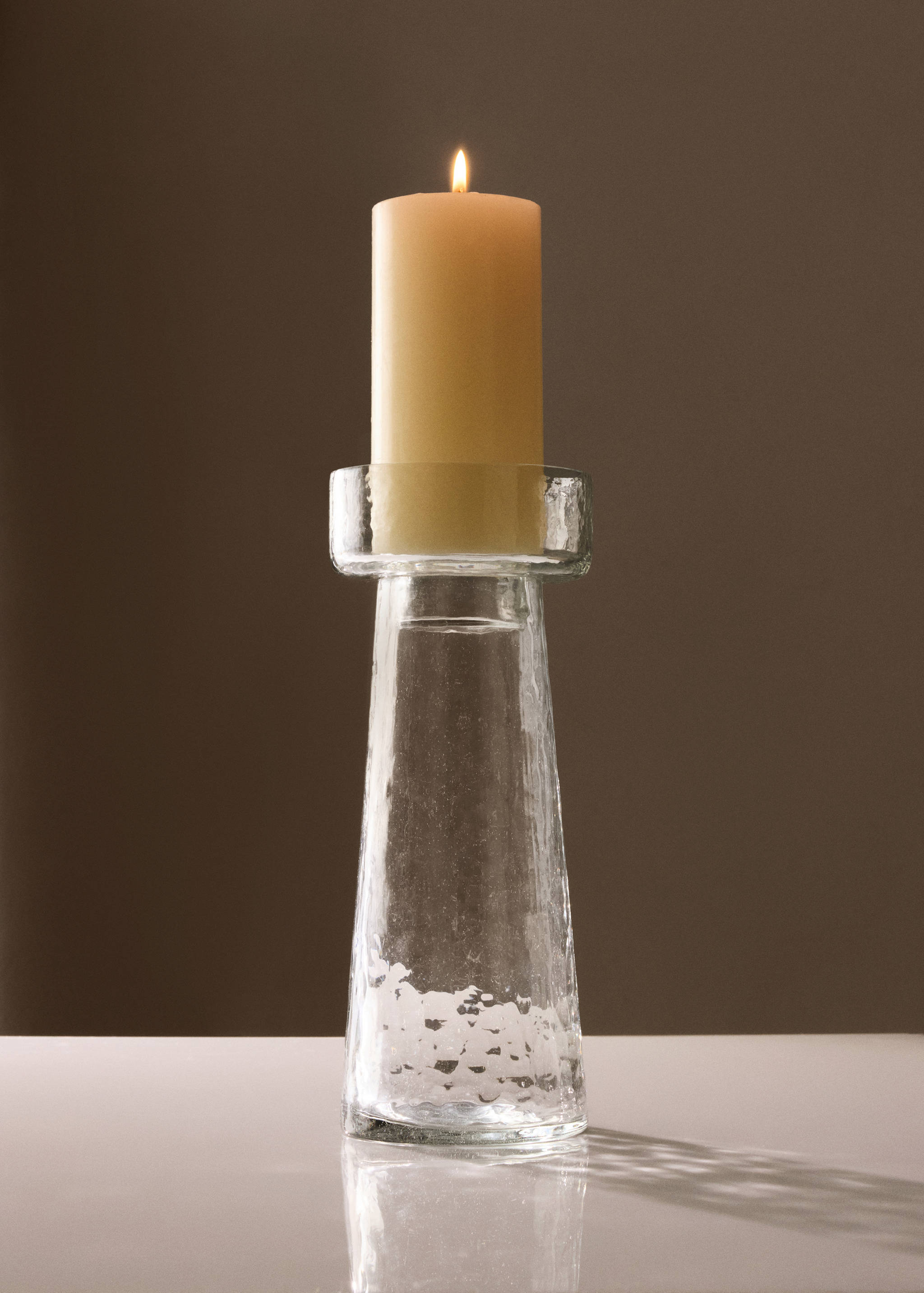 Clear glass candle holder holding a lit cream pillar candle.