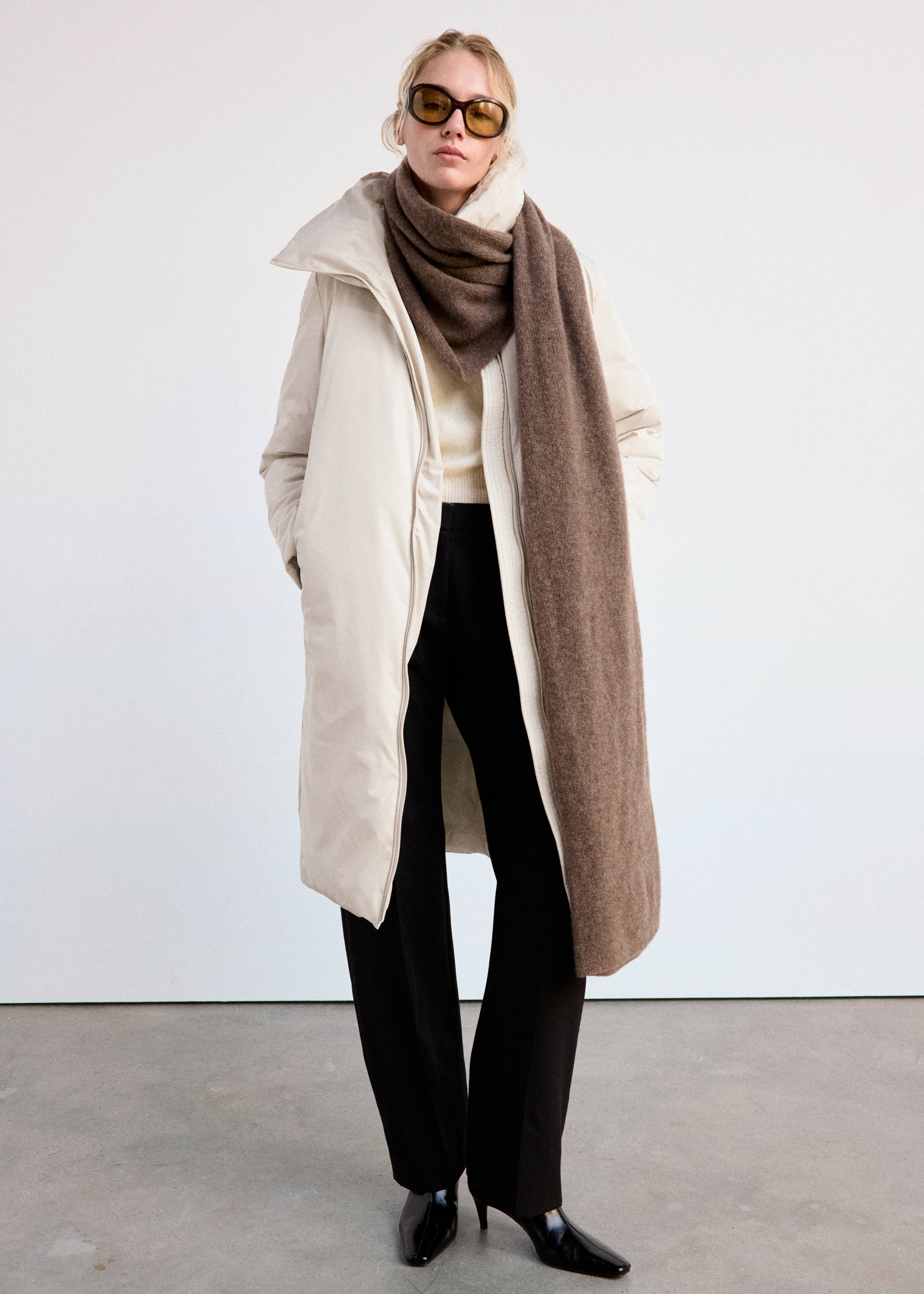 Long cream anorak with a high collar, styled with a brown scarf and black trousers.