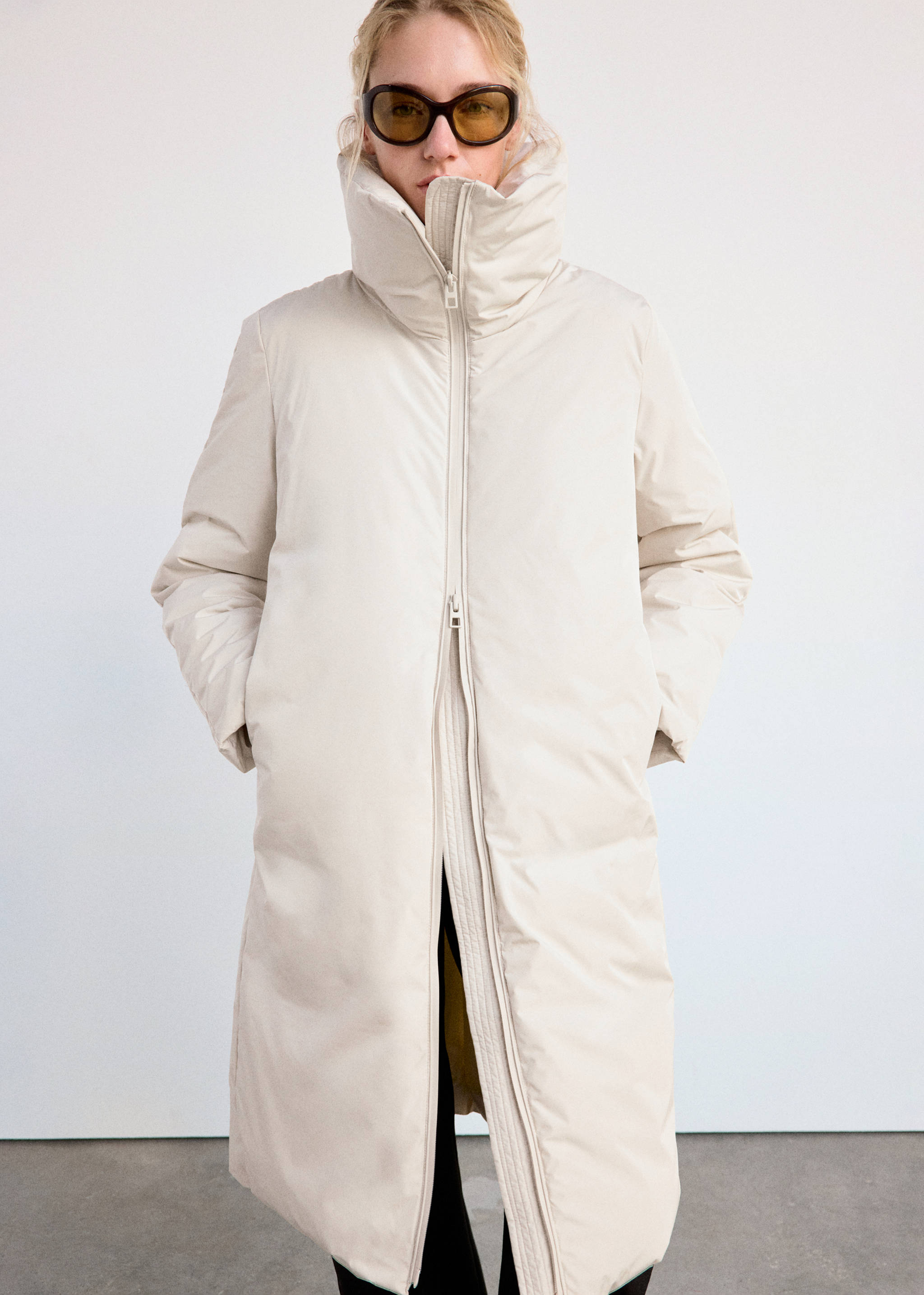 Off-white long anorak with high funnel neck and zip fastening.