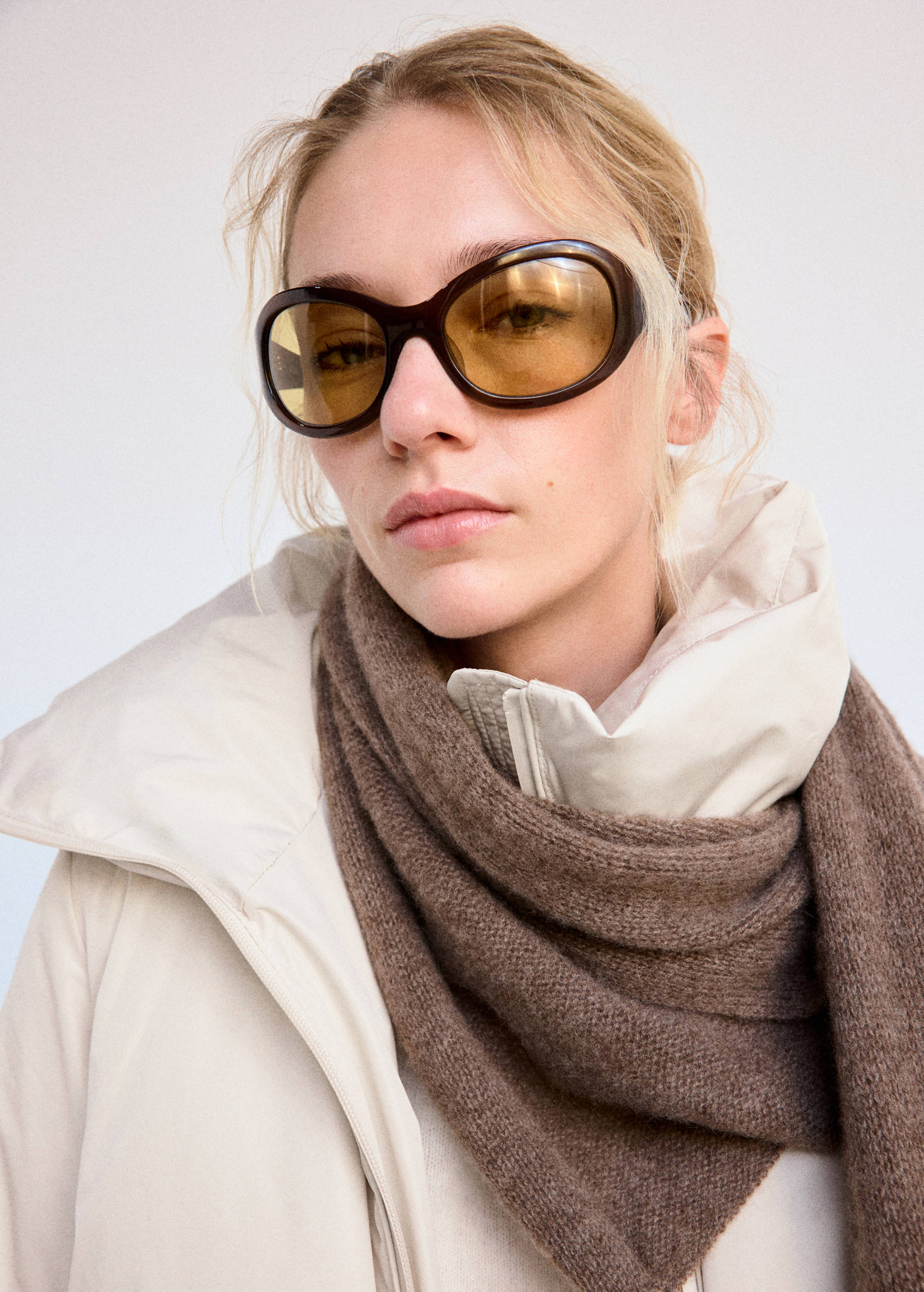 Close-up of a model wearing a light anorak with a high collar and a brown knitted scarf.