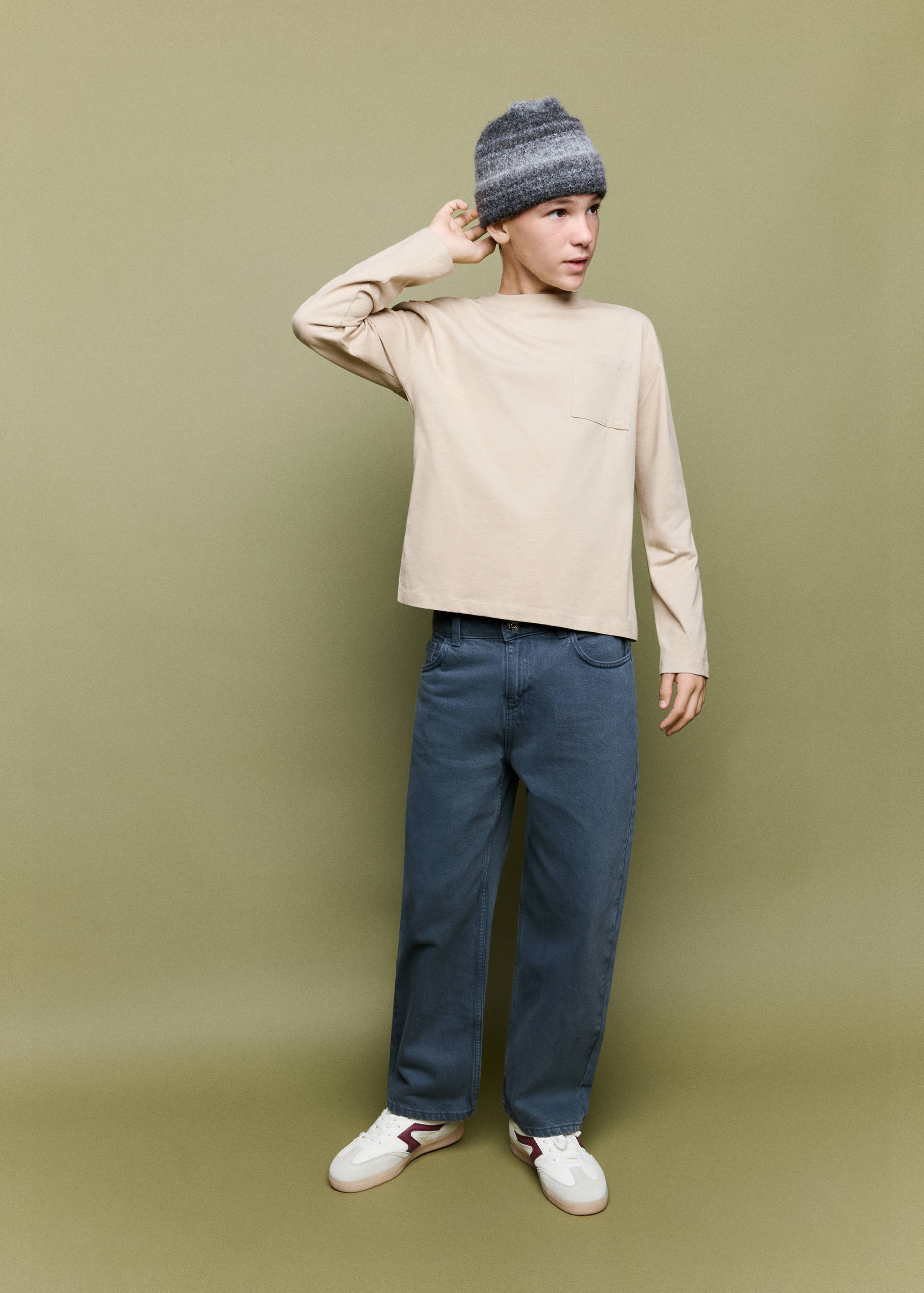 Beige long-sleeved t-shirt with a chest pocket, worn with grey trousers and a beanie.