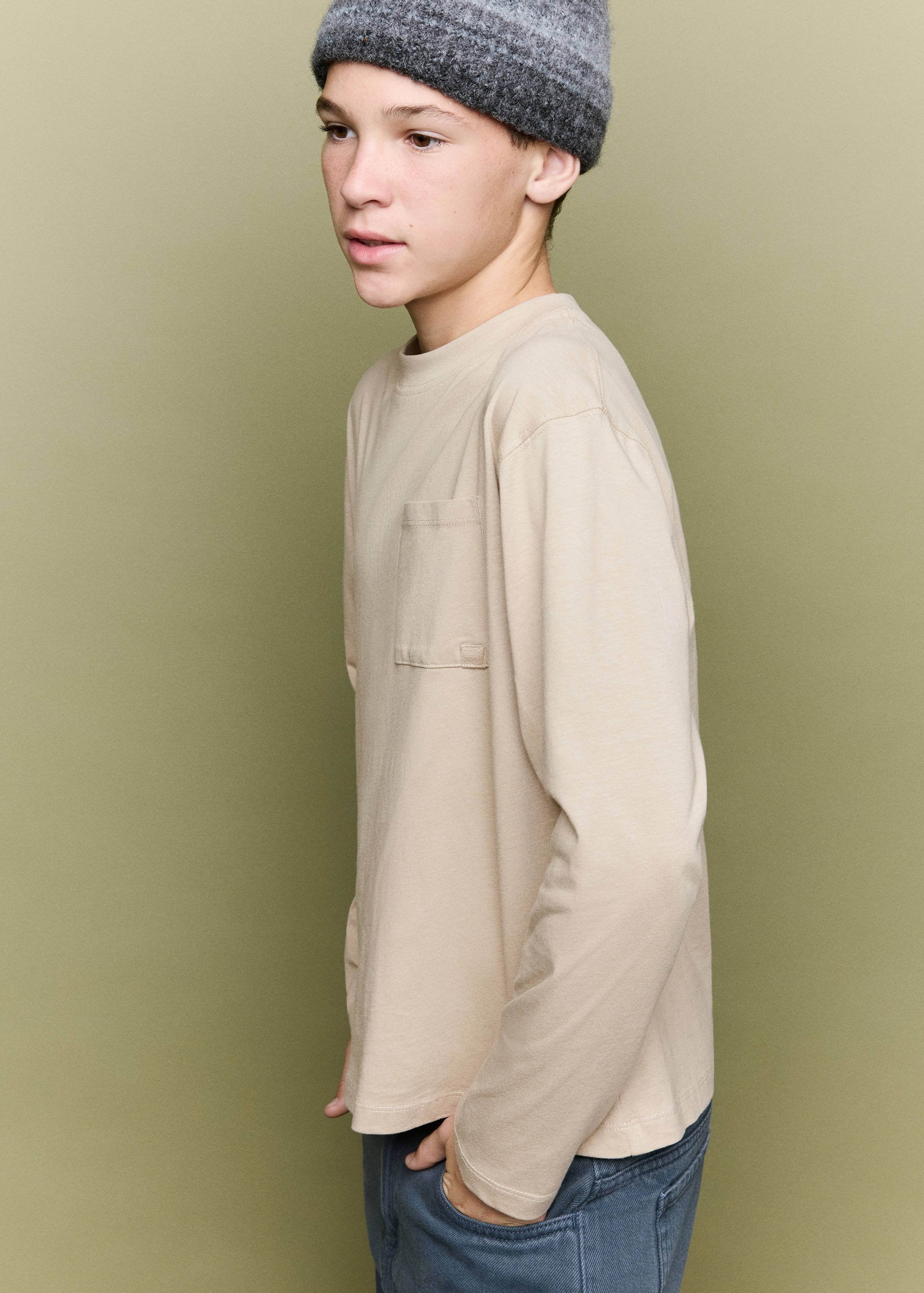 Beige long-sleeved t-shirt with crew neck and chest pocket, shown on a model.