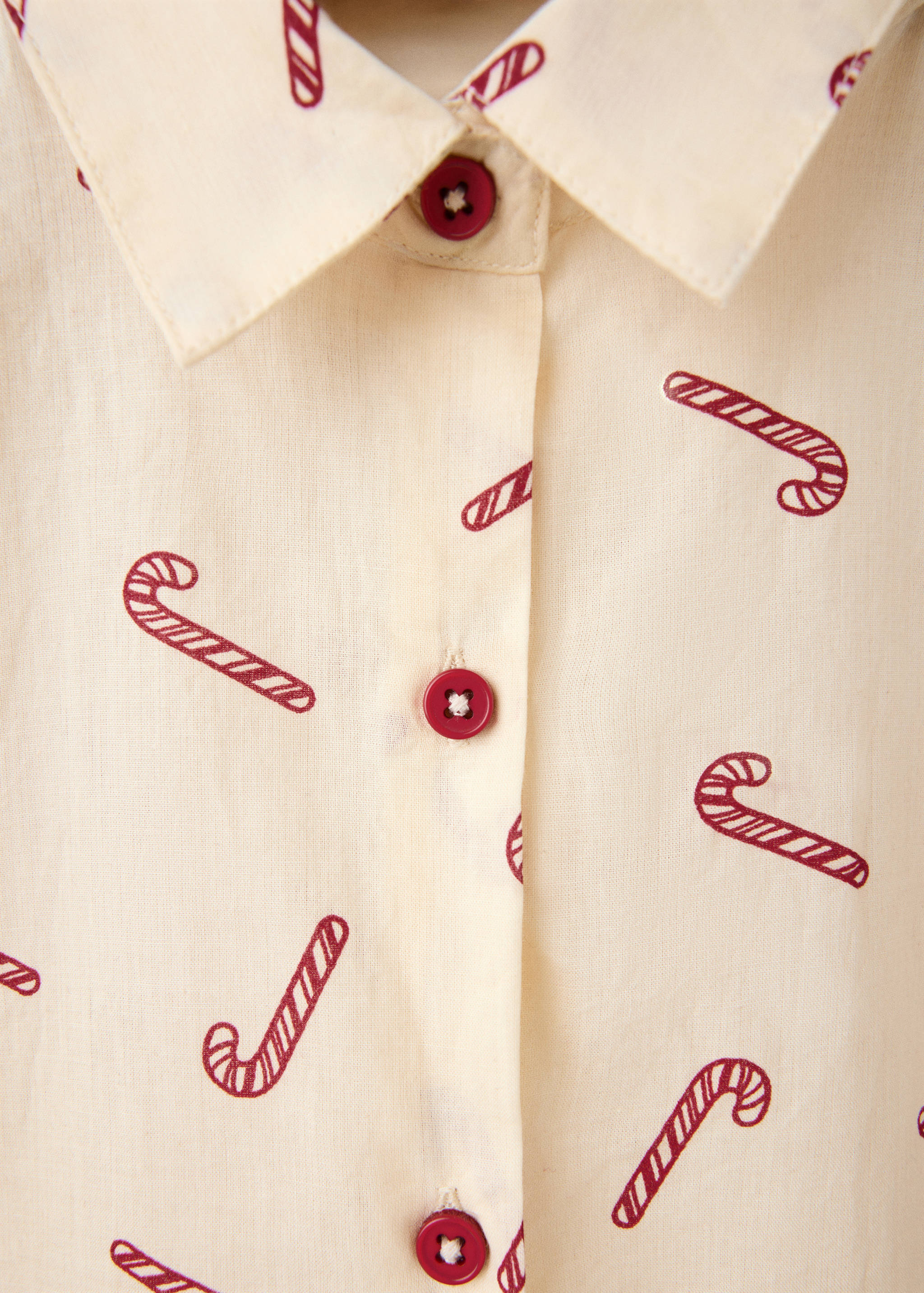 Close-up of a beige pyjama shirt with a red candy cane print and buttons.