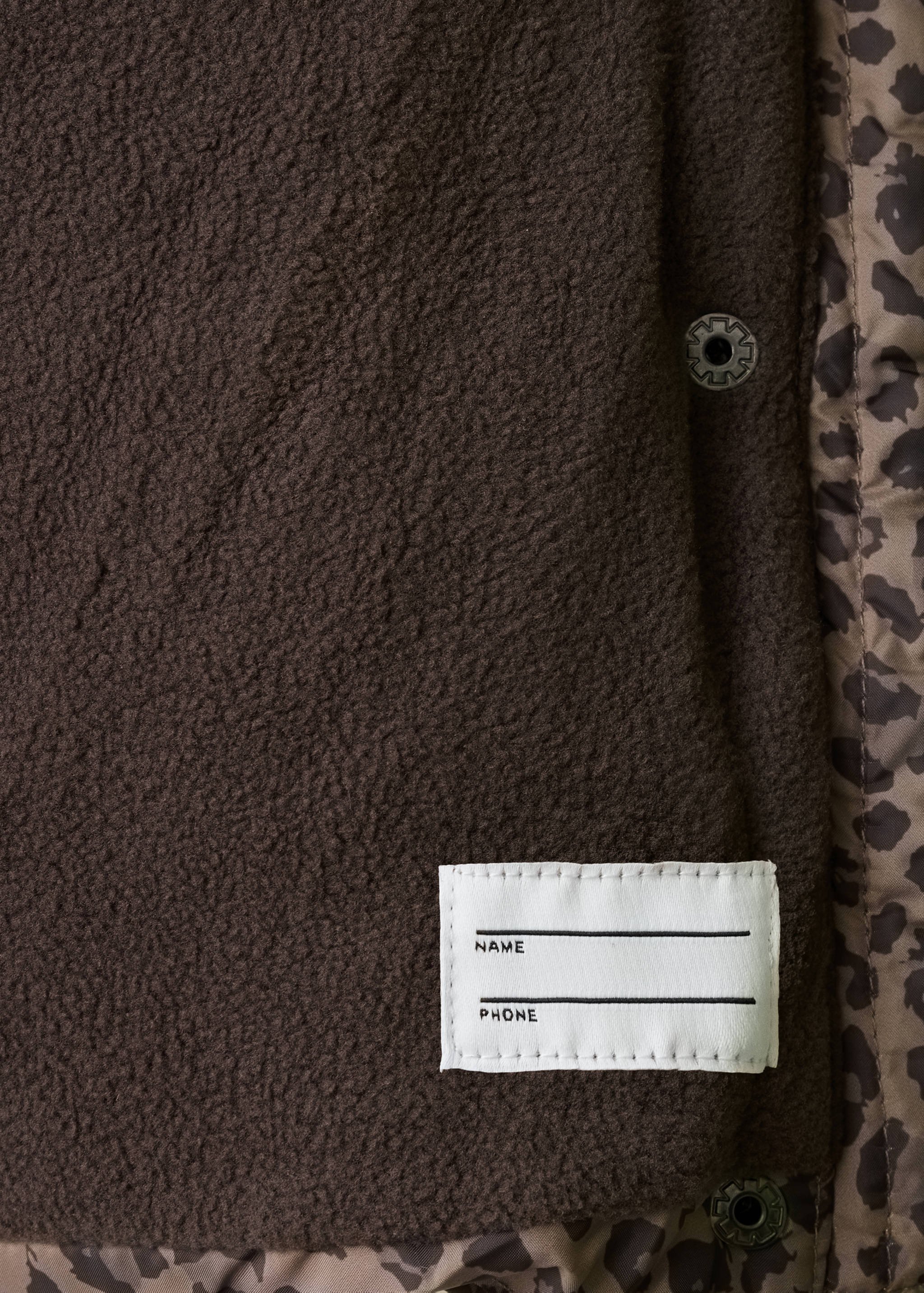 Close-up of the brown anorak's fleece lining, leopard-print trim, and name label.