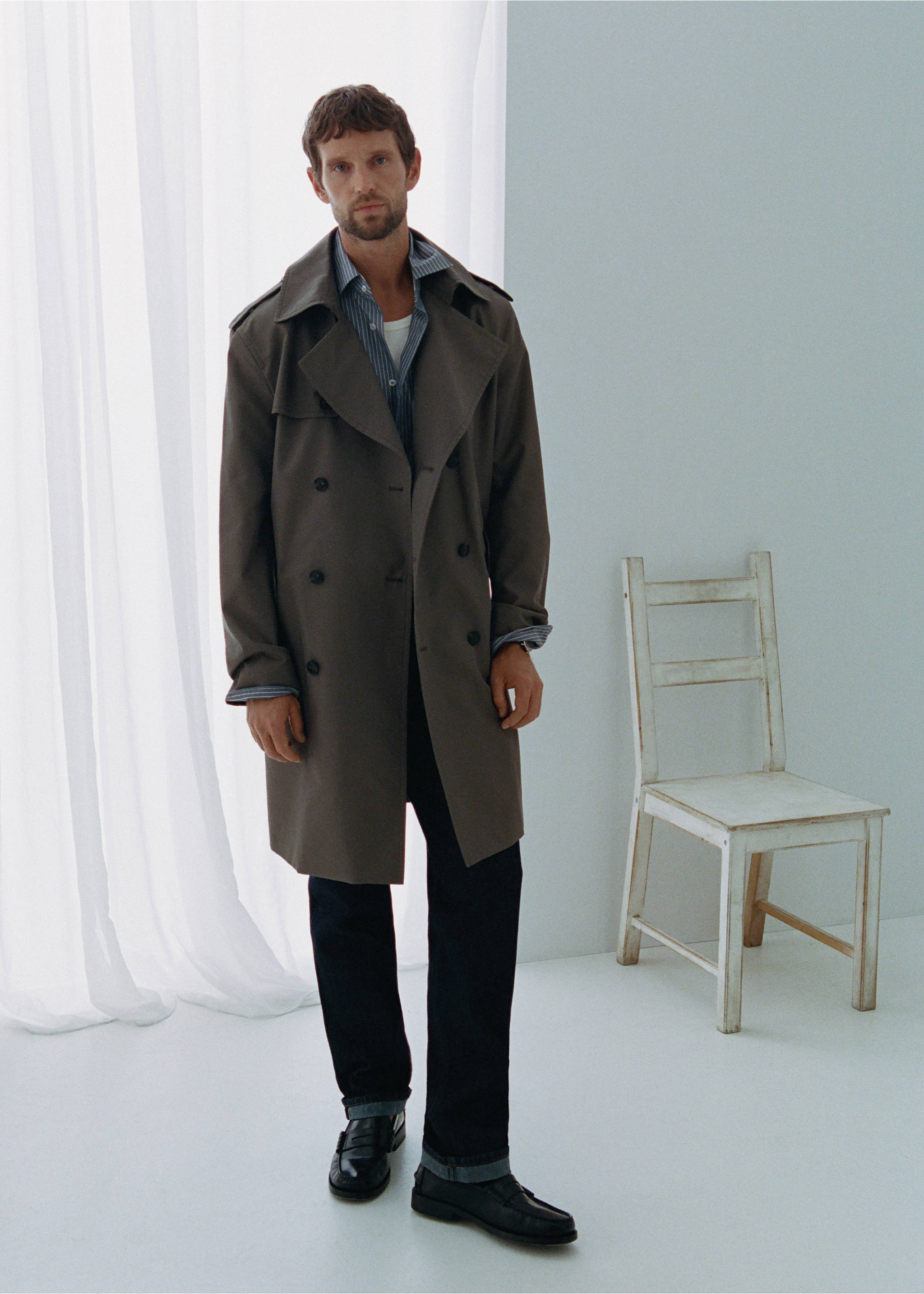 Dark grey double-breasted trench coat with wide lapels worn over a striped shirt and dark blue jeans., Open Blue. Ref: 37045974-00.