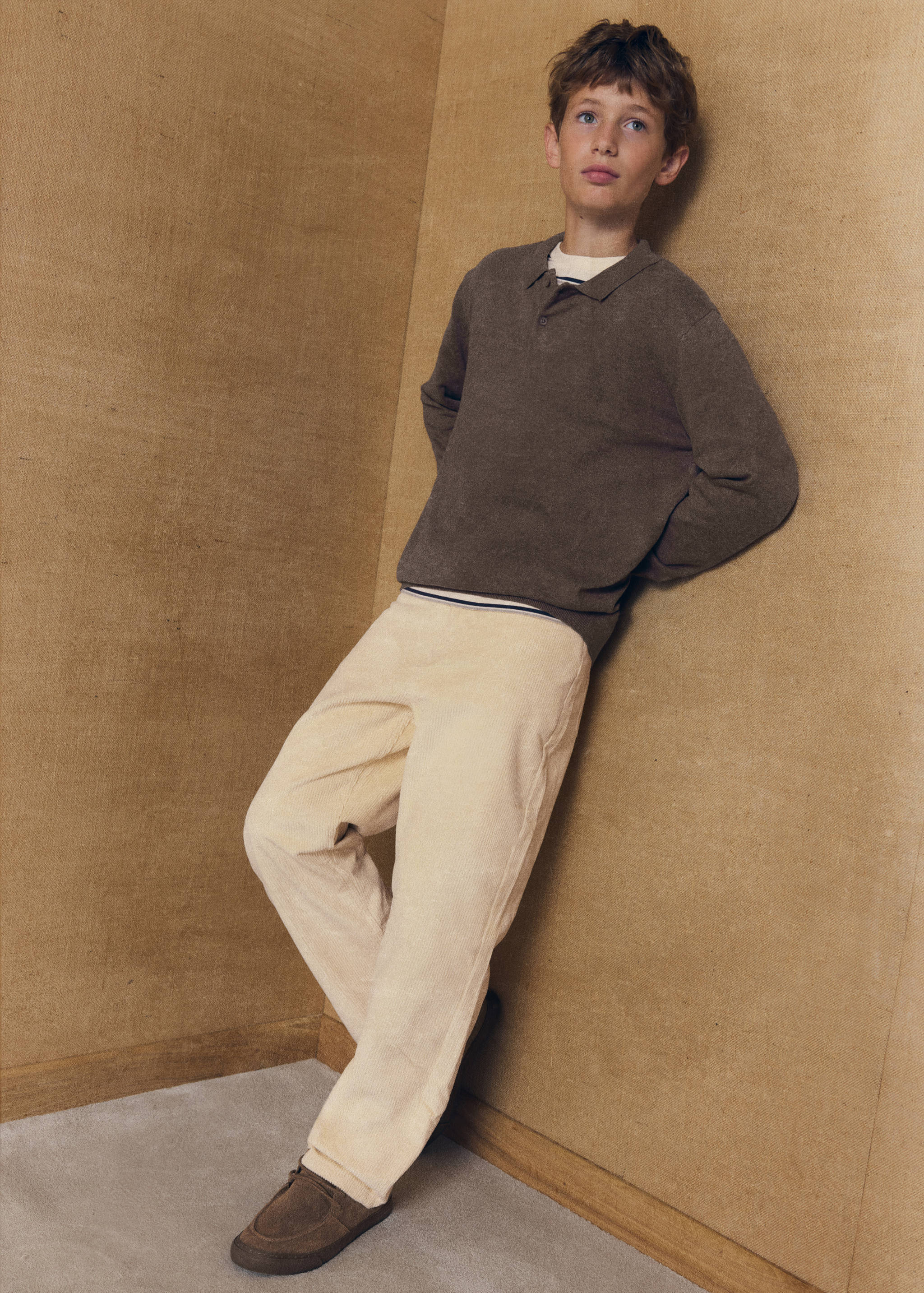 Cream trousers in a straight fit, worn with a brown polo shirt.
