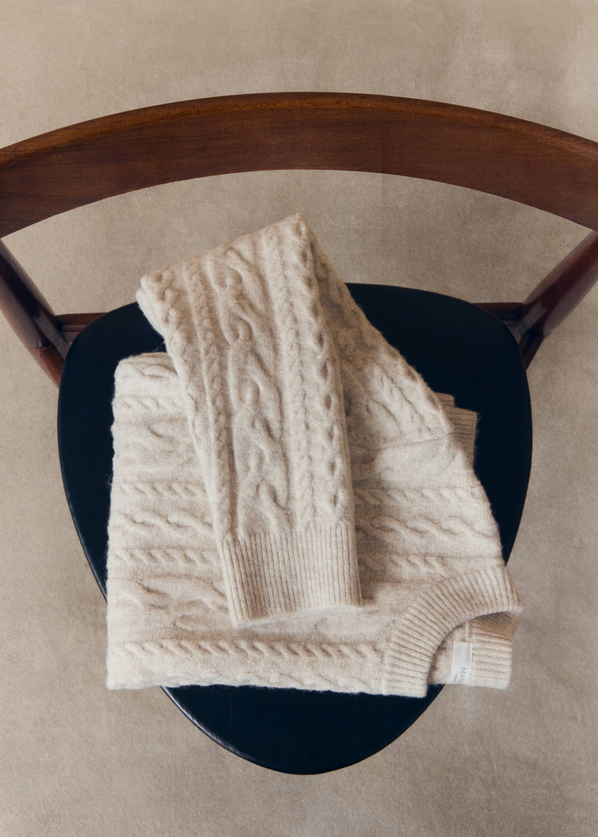 Cream cable-knit jumper folded on a chair.