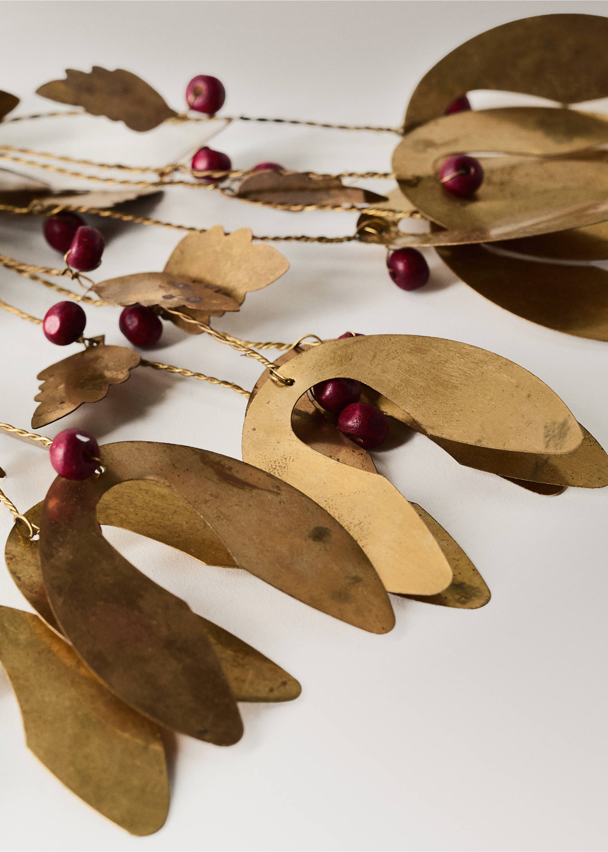 Close-up of a gold brass decorative garland with leaf shapes and red berries., Gold. Ref: 37046736-00.