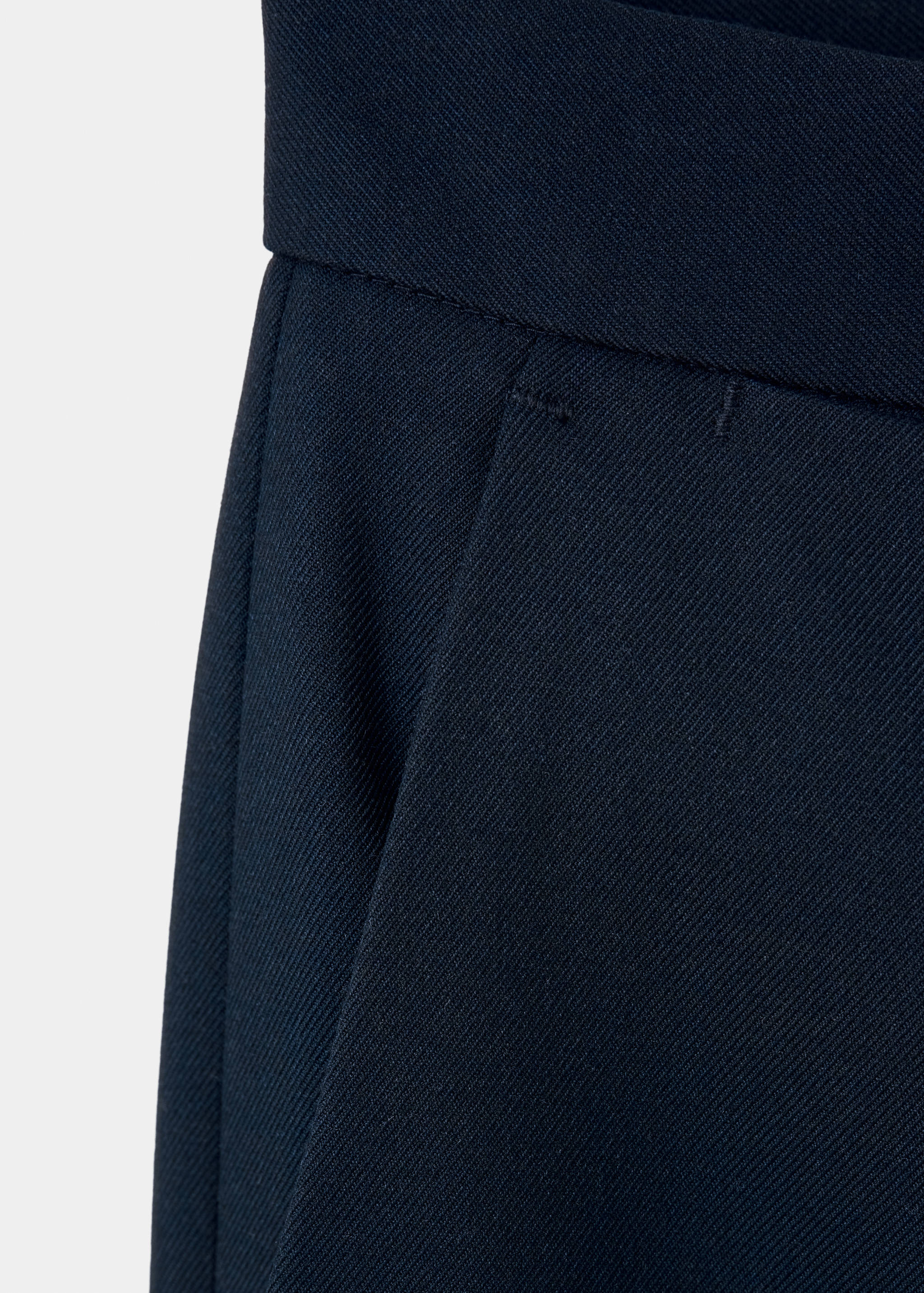 Close-up of the waistband and pocket on dark navy blue trousers.