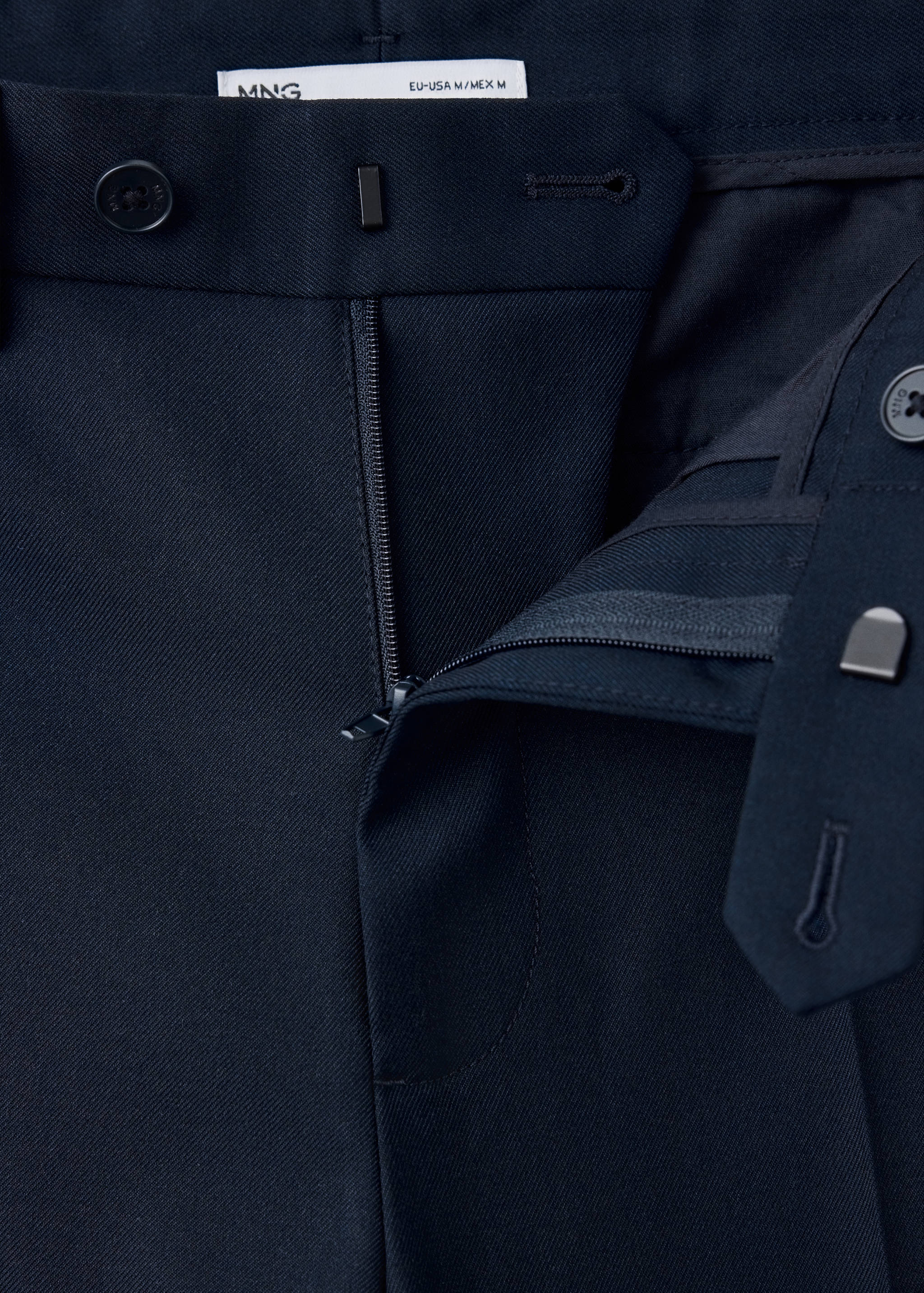 Close-up of the waistband and zip closure on dark navy blue twill trousers.