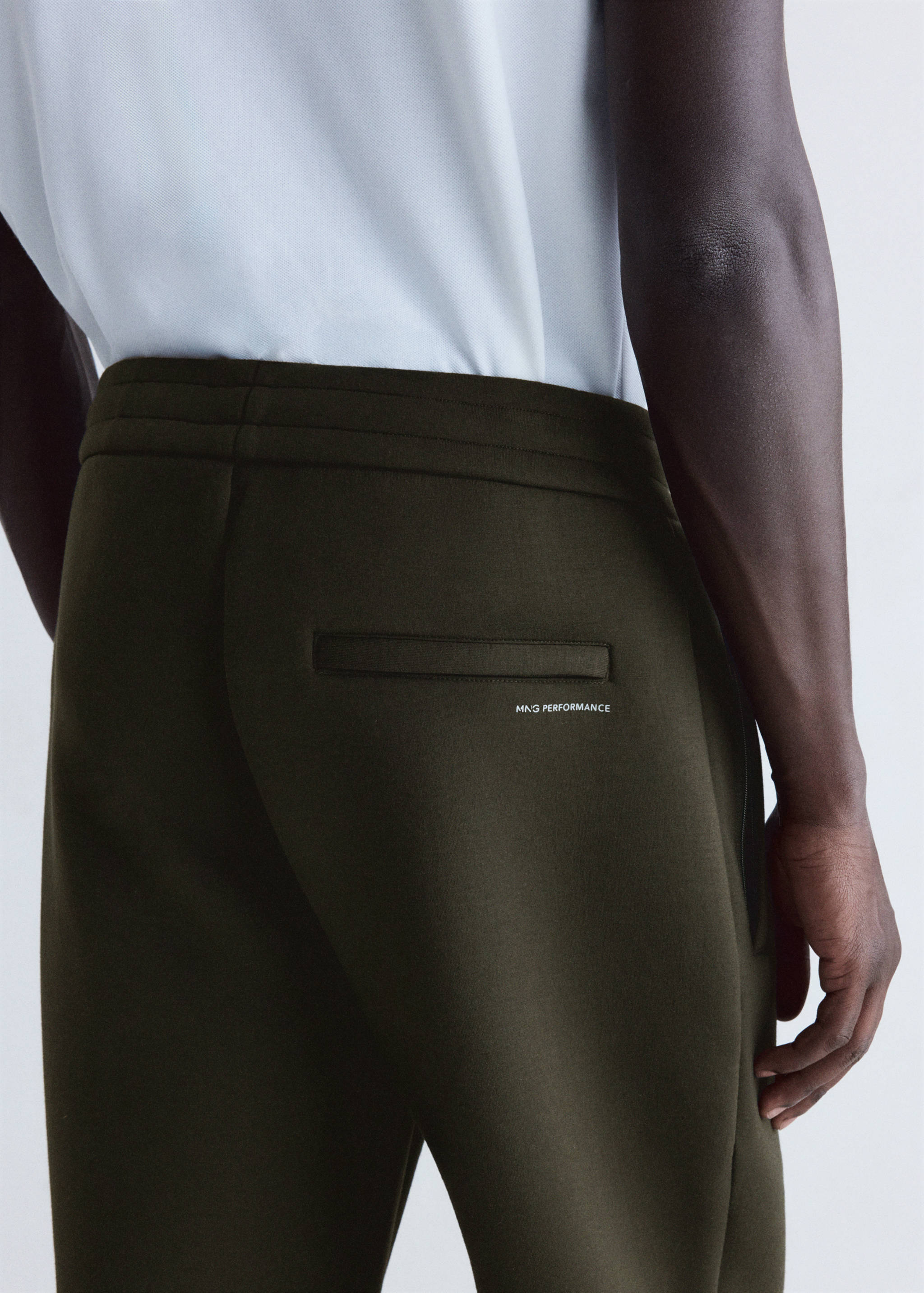 Joggers en verde caqui oscuro con un bolsillo trasero y estampado MNG PERFORMANCE en blanco, vista trasera.