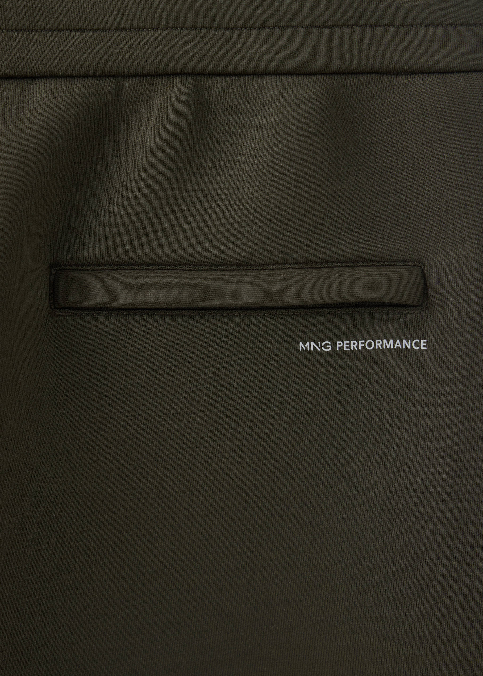 Detalle de tejido de joggers en verde oscuro con un bolsillo y el texto MNG PERFORMANCE.