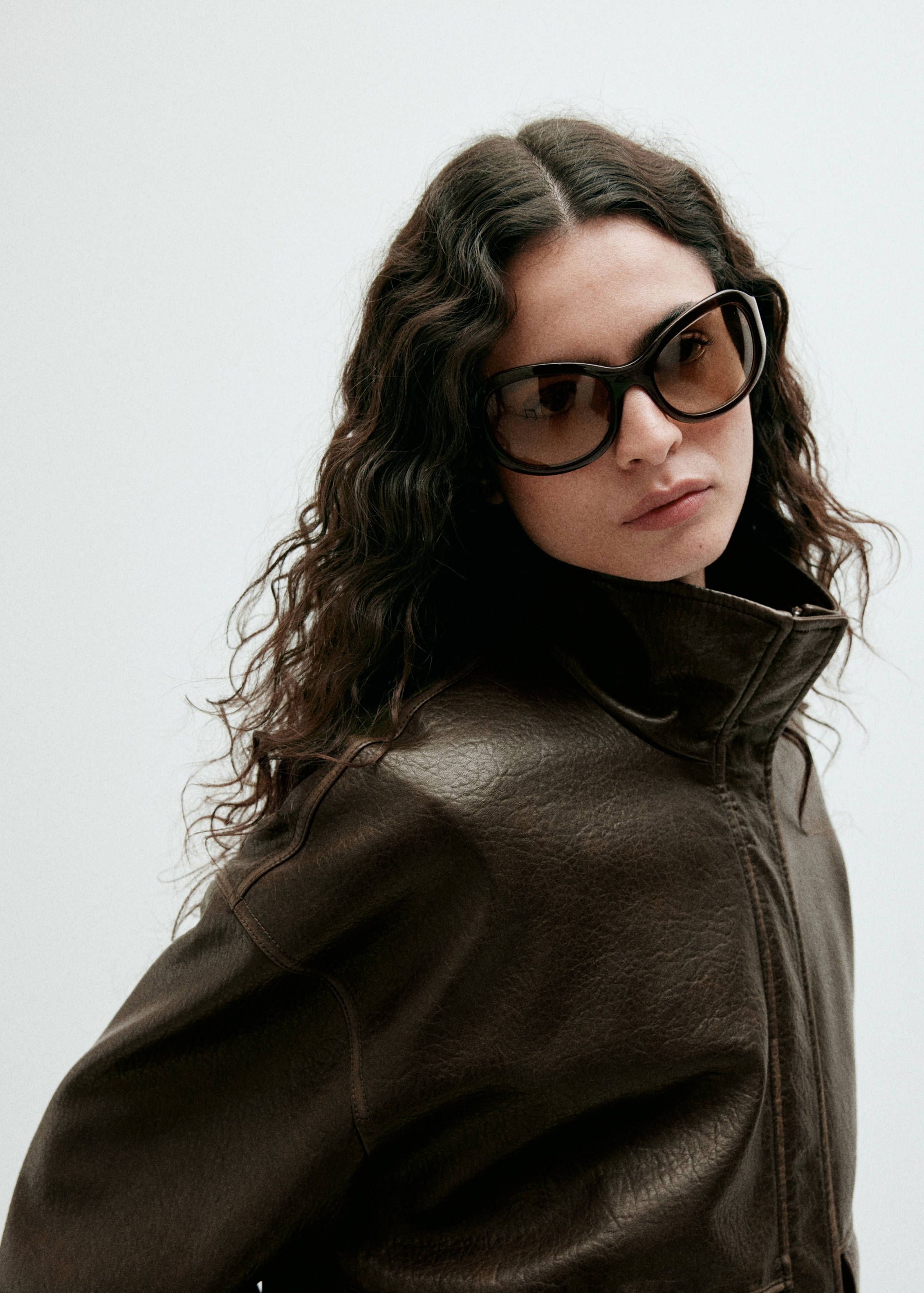 Dark brown leather jacket with high collar worn with sunglasses.