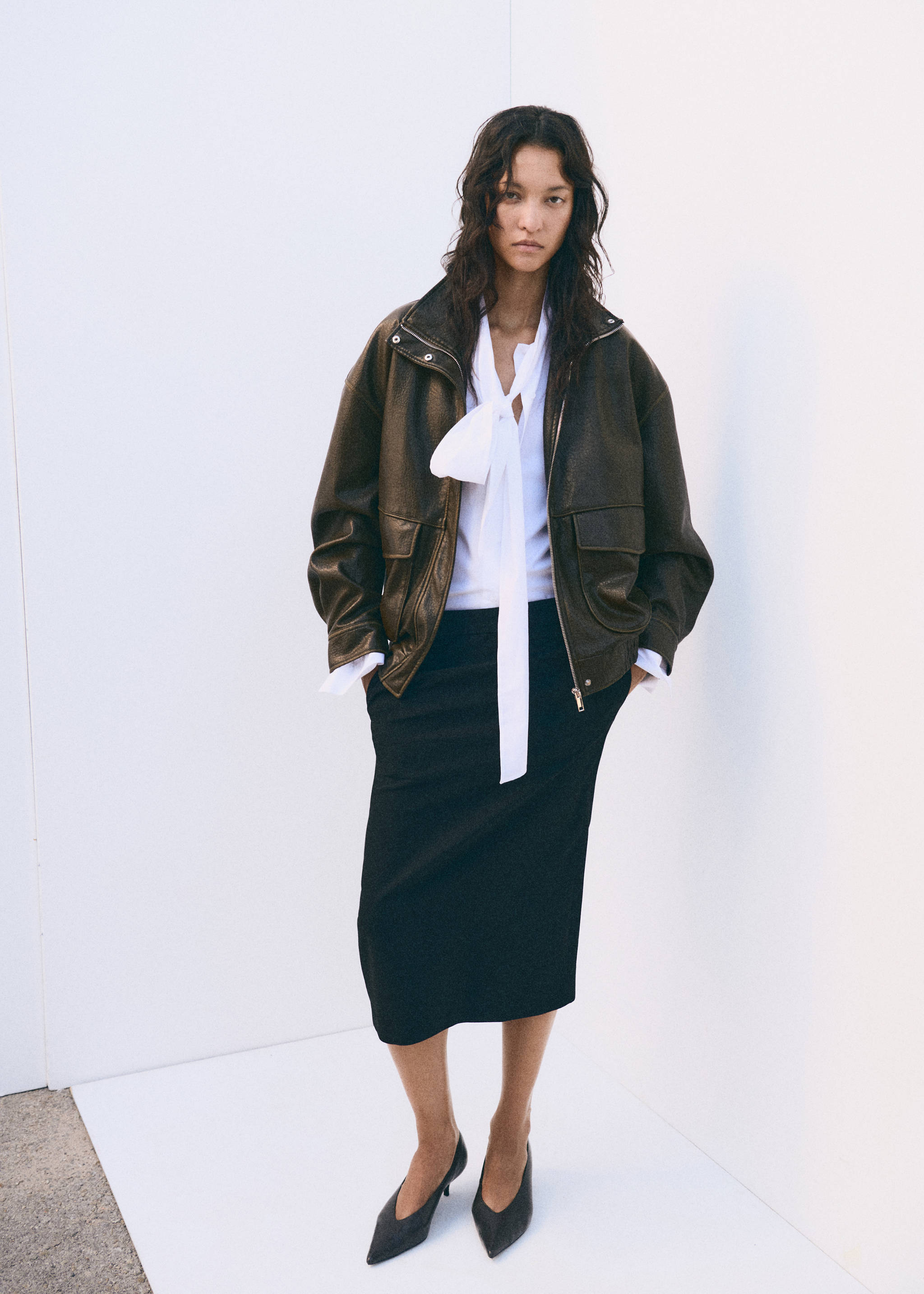 Dark brown leather jacket styled with a white blouse and black midi skirt.