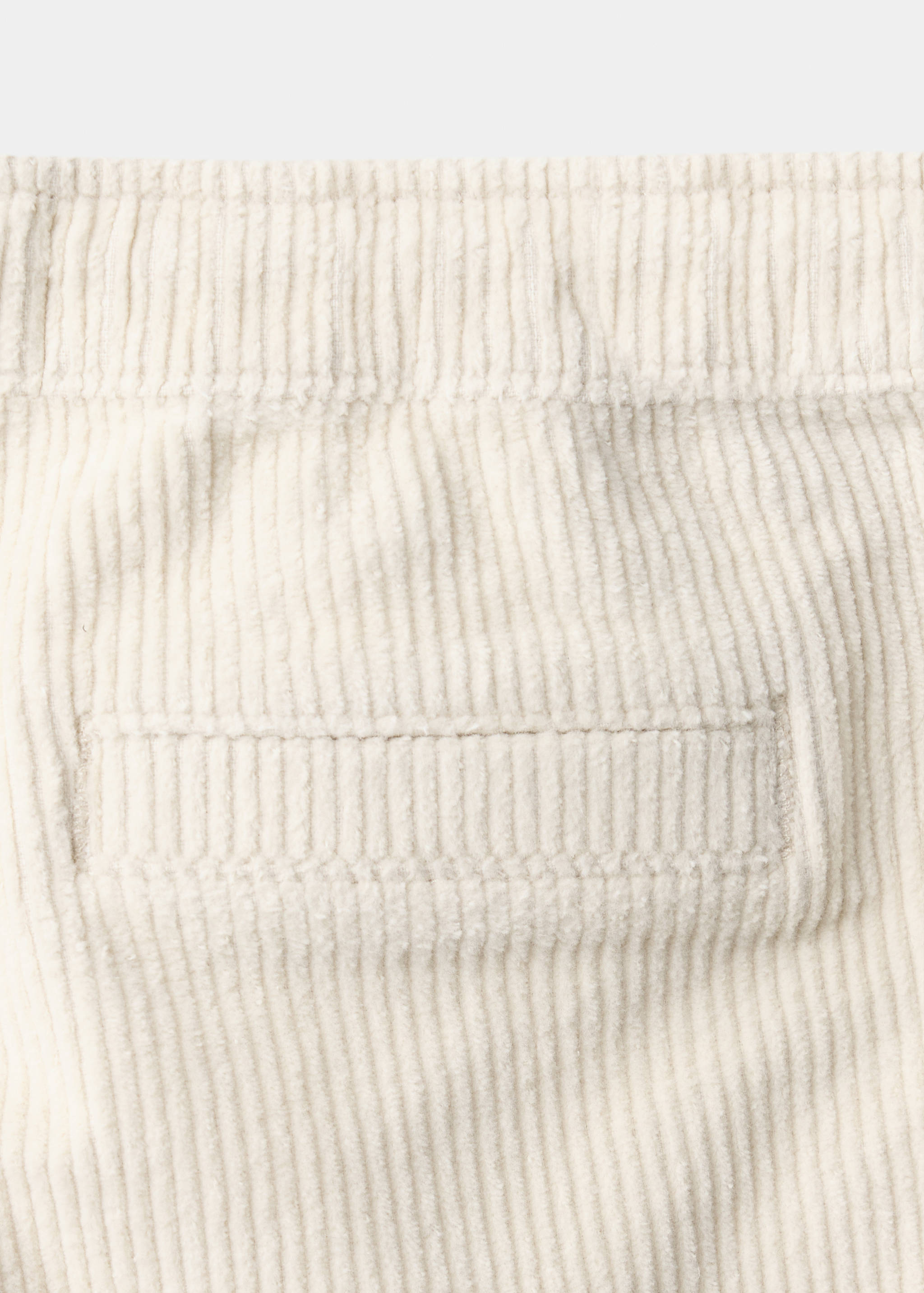 Off-white corduroy texture detail on trousers.