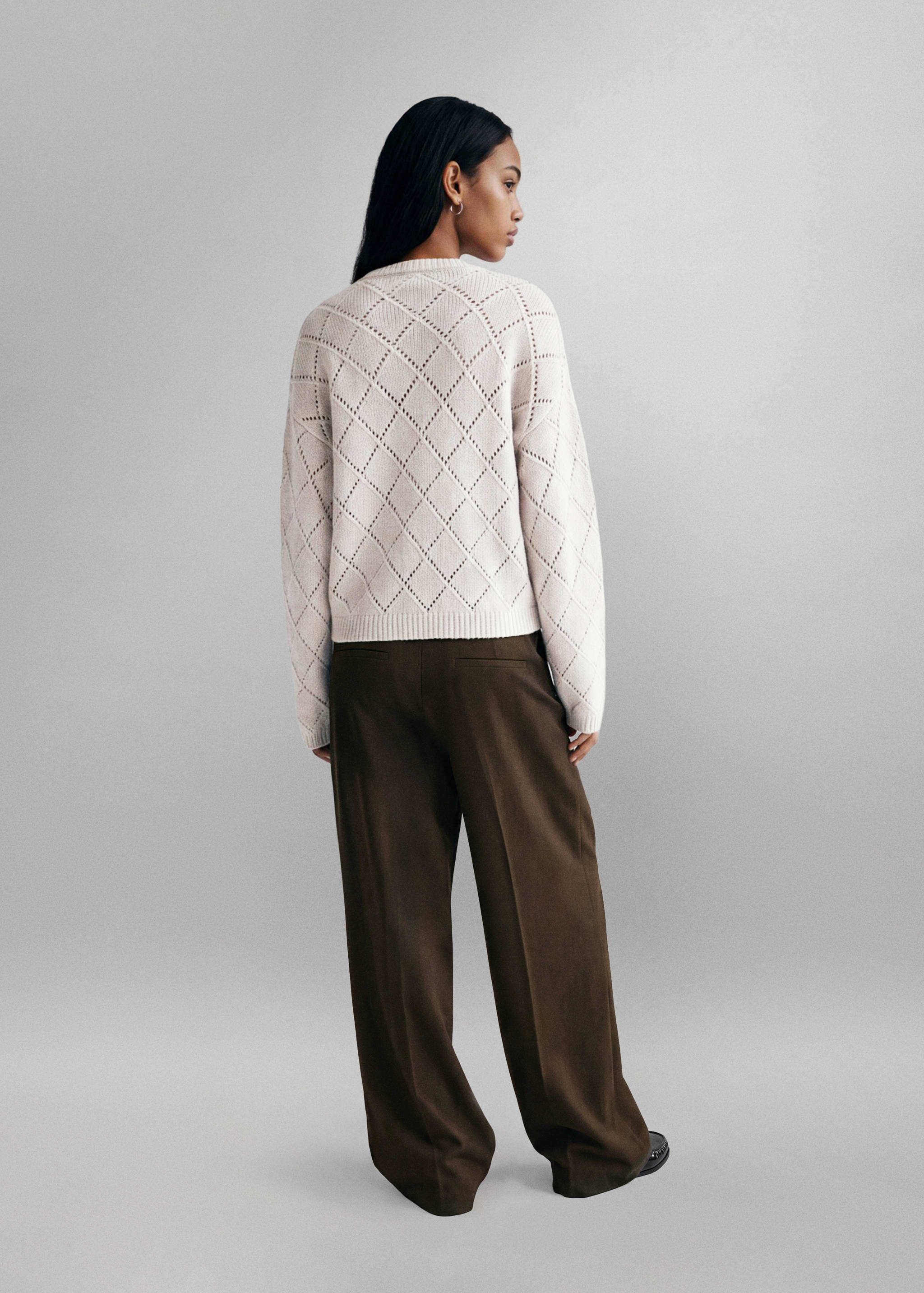 Off-white knitted diamond-pattern jersey from the back, worn with dark trousers