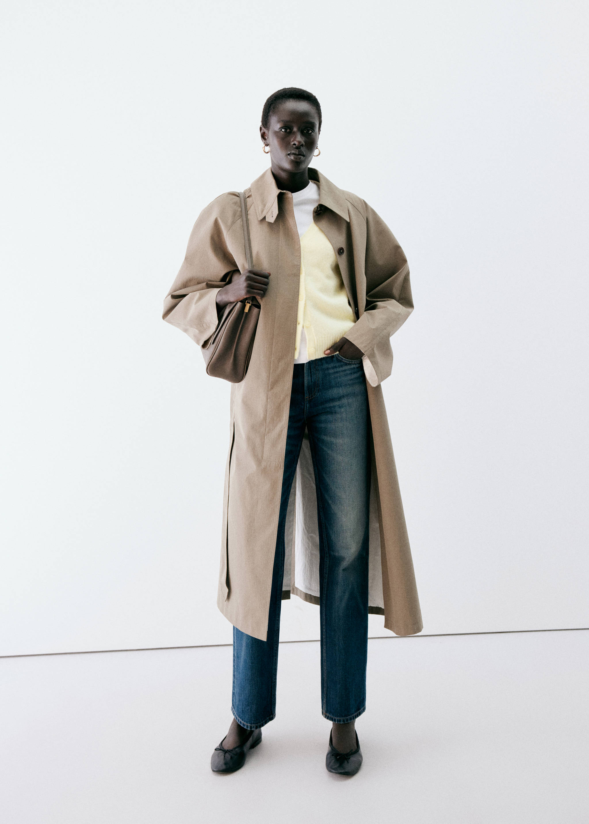 Pale yellow cardigan layered under an open beige trench coat with blue jeans.