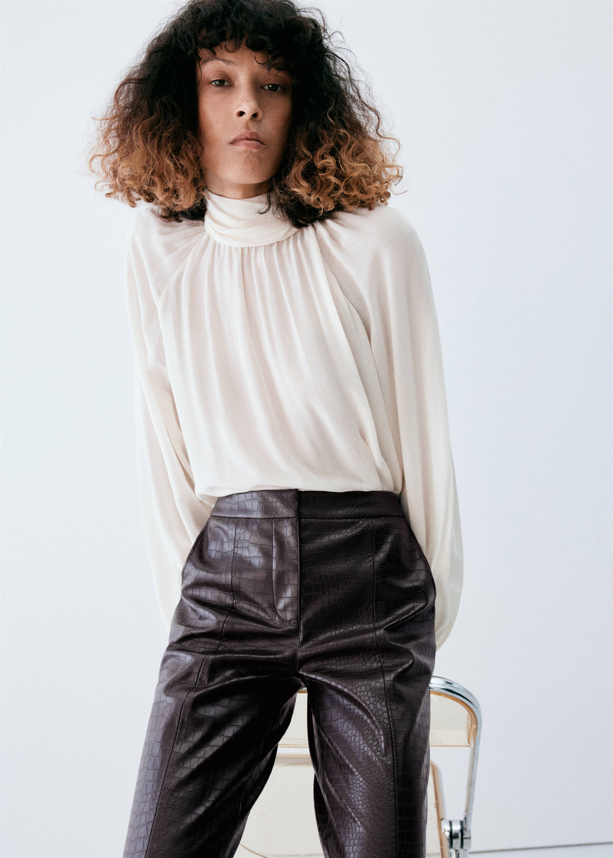 Dark brown crocodile-embossed trousers worn with a cream high-neck blouse.