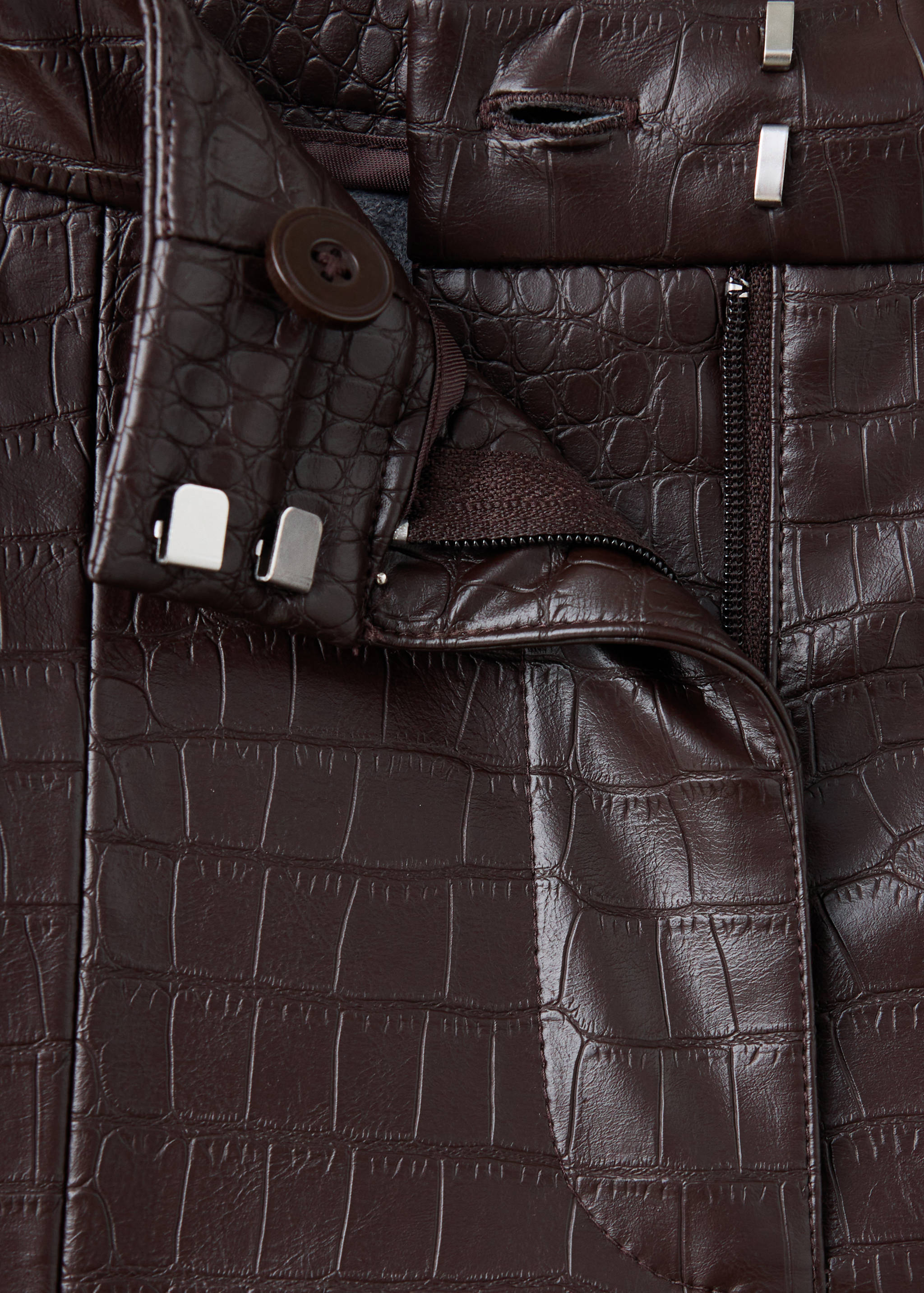 Close-up of dark brown crocodile-embossed trousers waistband.