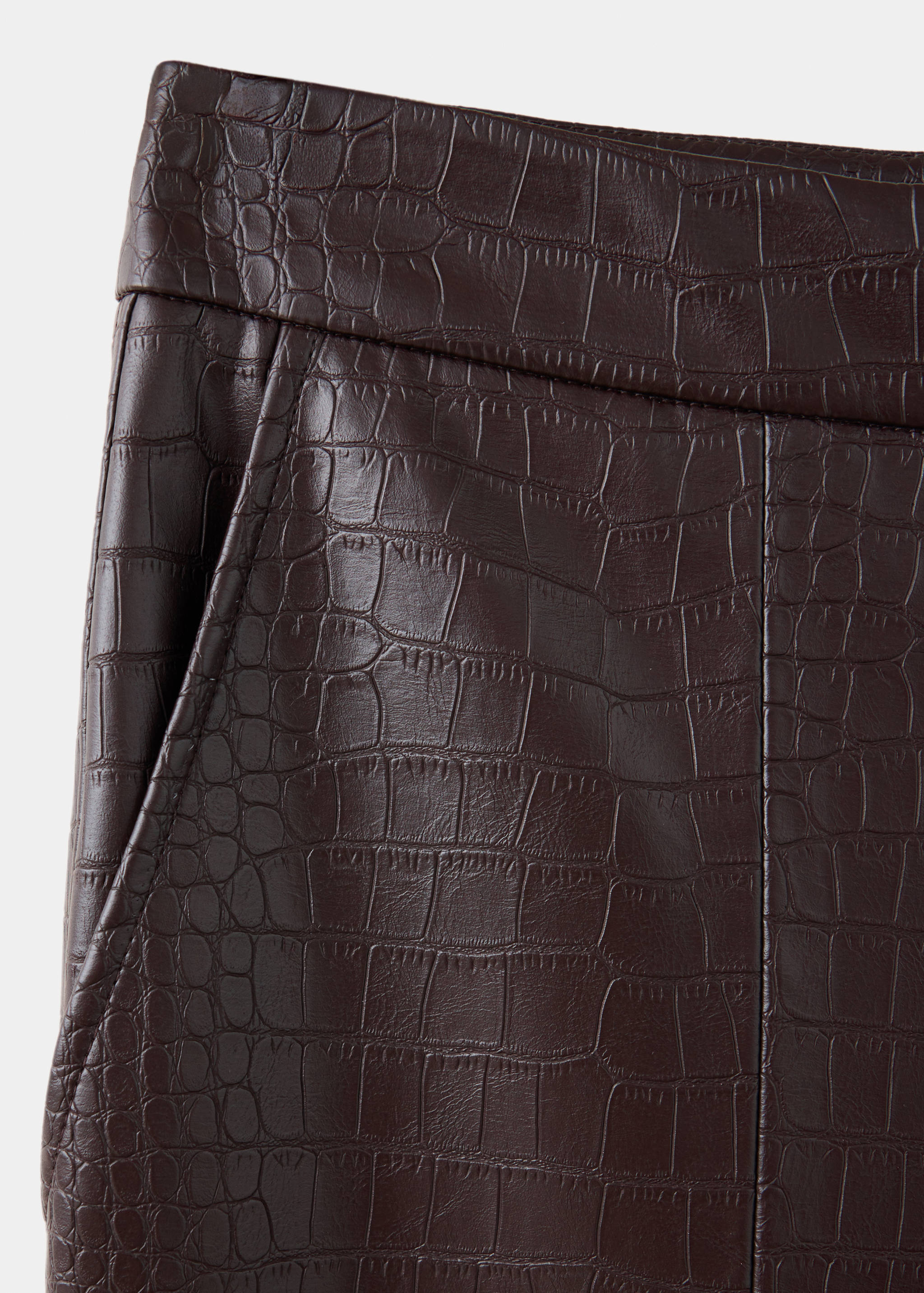 Close-up of dark brown crocodile-embossed trousers fabric texture.