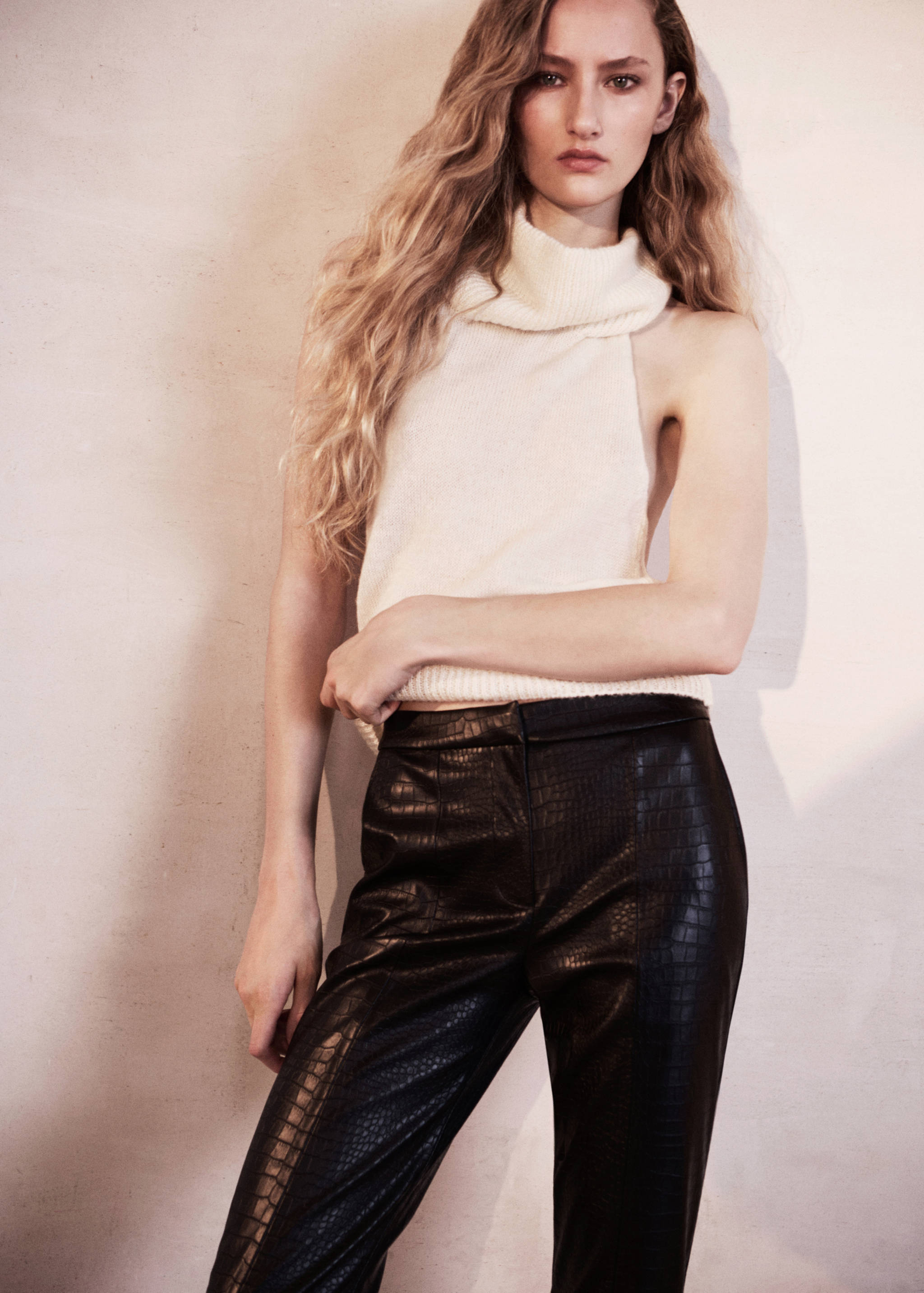 Black crocodile-effect trousers worn with a white high-neck knit top.