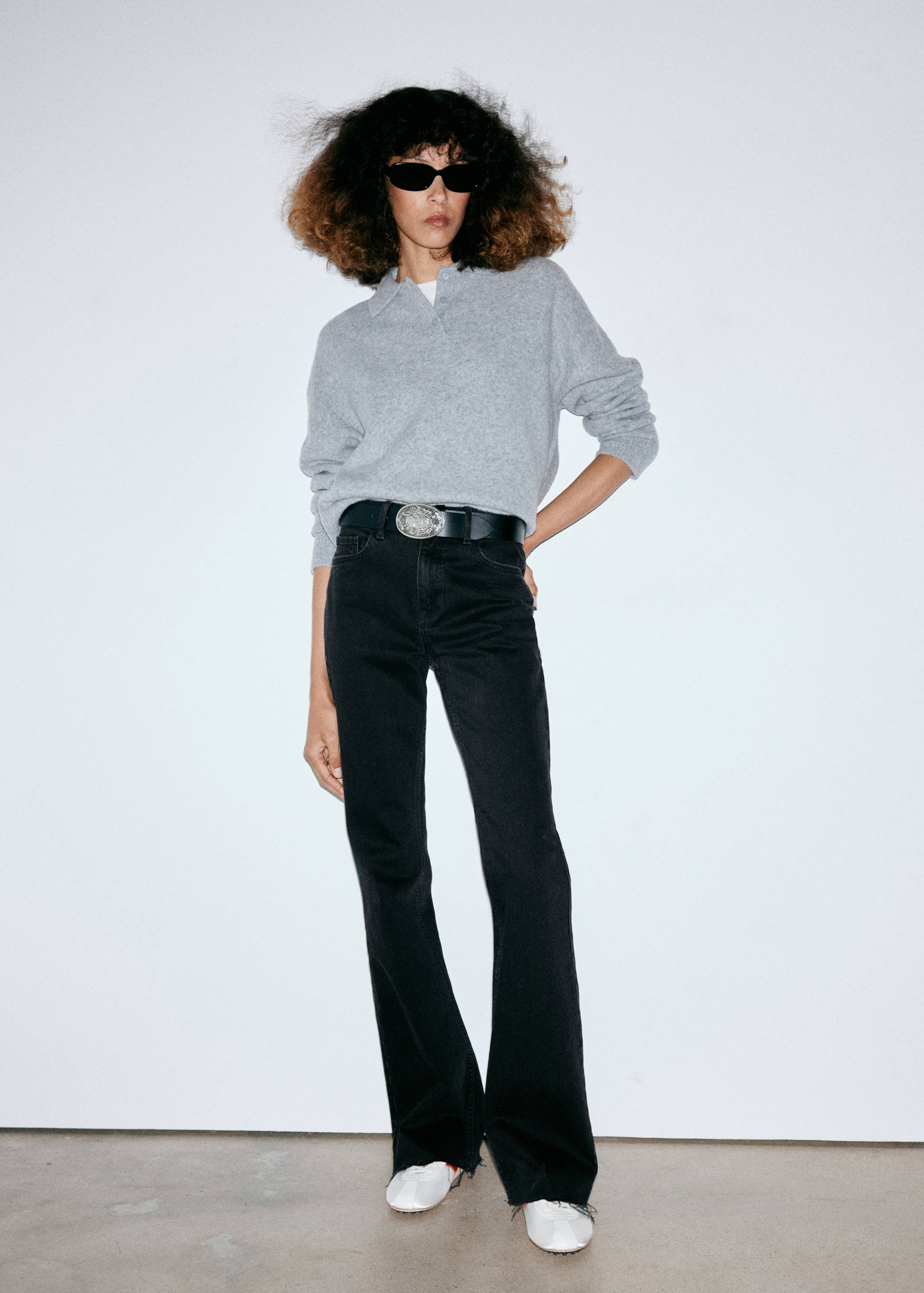 Black flare jeans worn with a grey polo sweater and a statement belt.