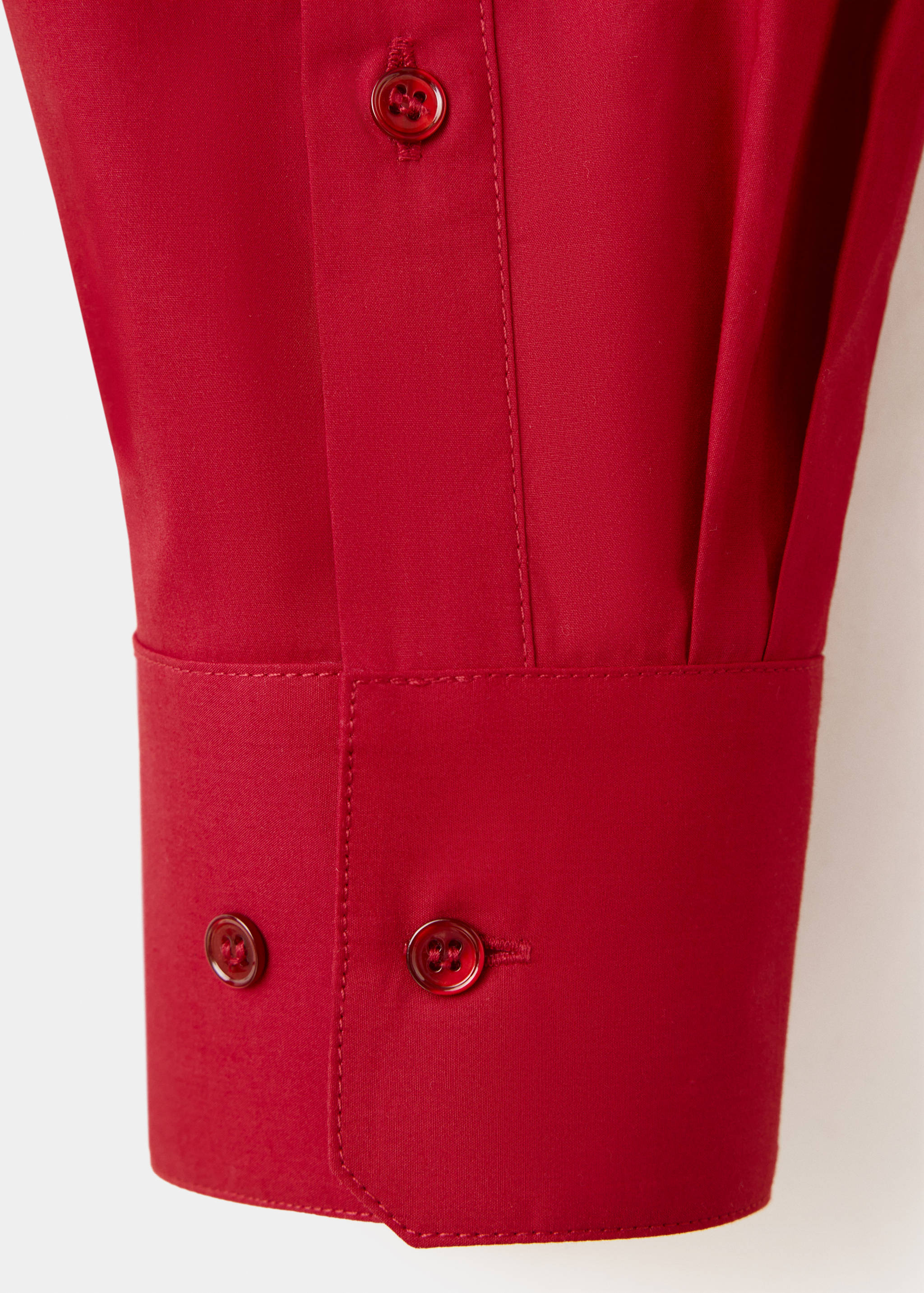 Close-up of a red shirt cuff with matching buttons and tonal stitching.