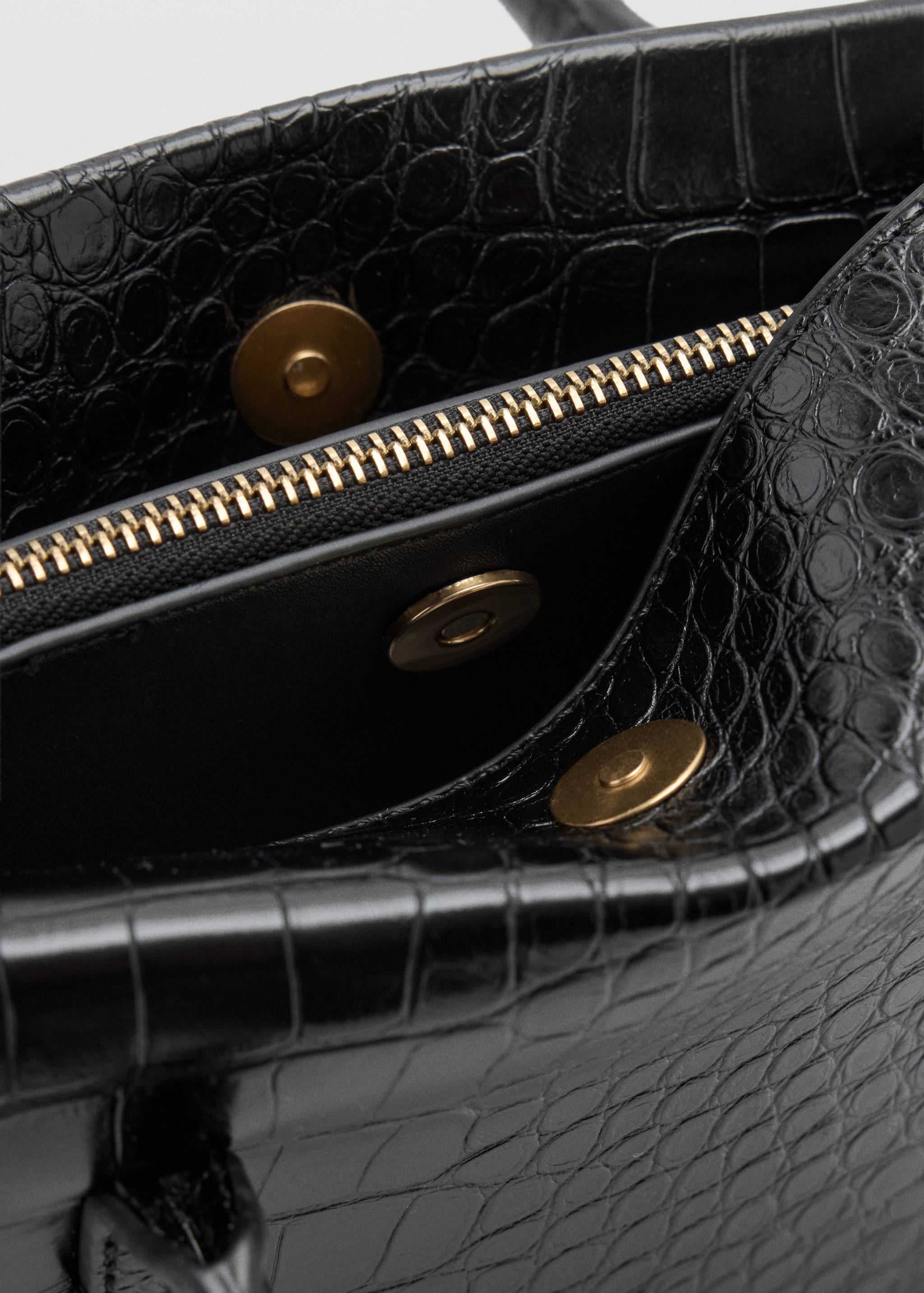 Close-up of a black crocodile-effect shoulder bag with gold-toned zipper and snap fasteners.