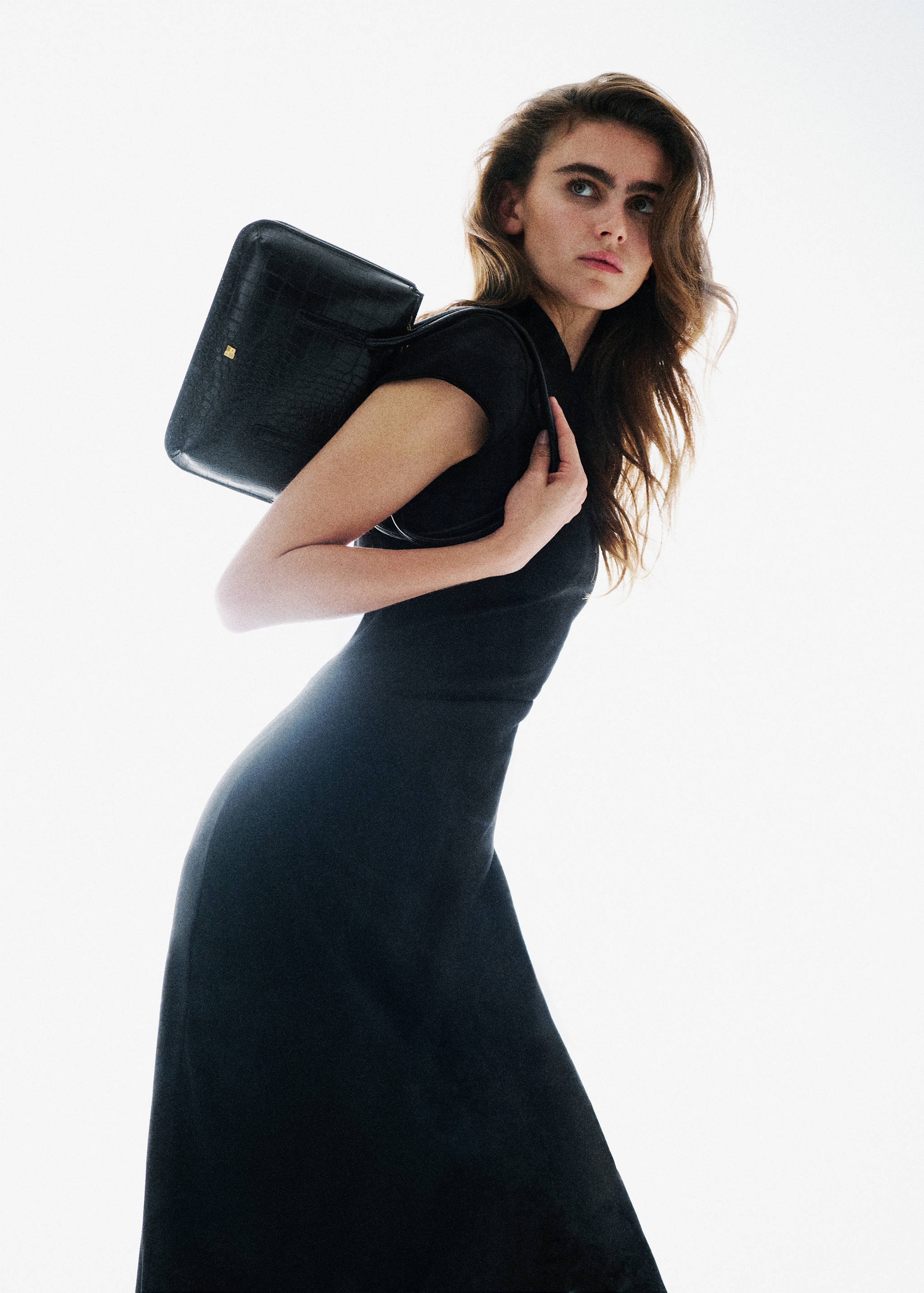 Black embossed shoulder bag worn by a model in a black dress.