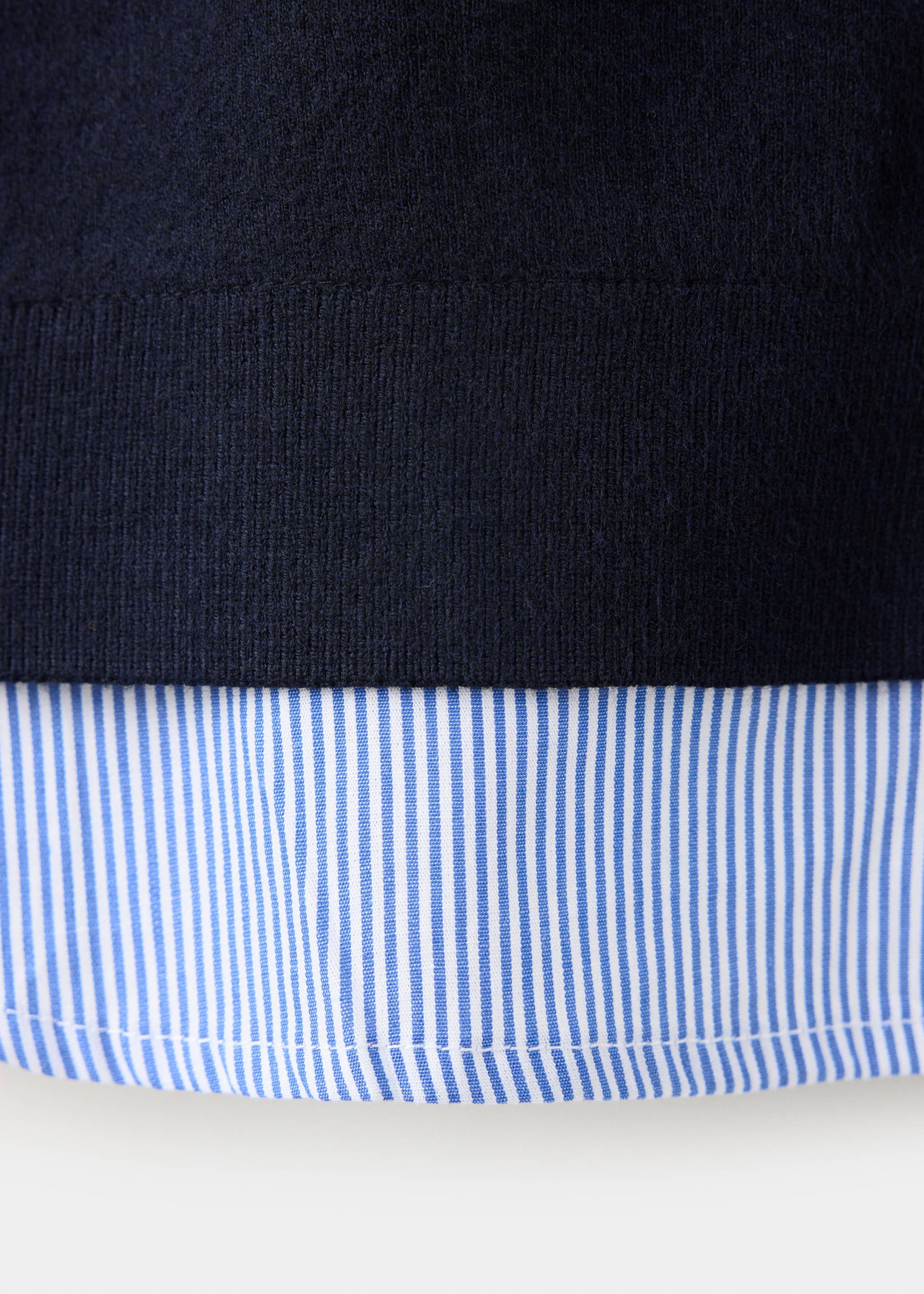 Close-up of navy knit jacket with layered striped shirt hem.