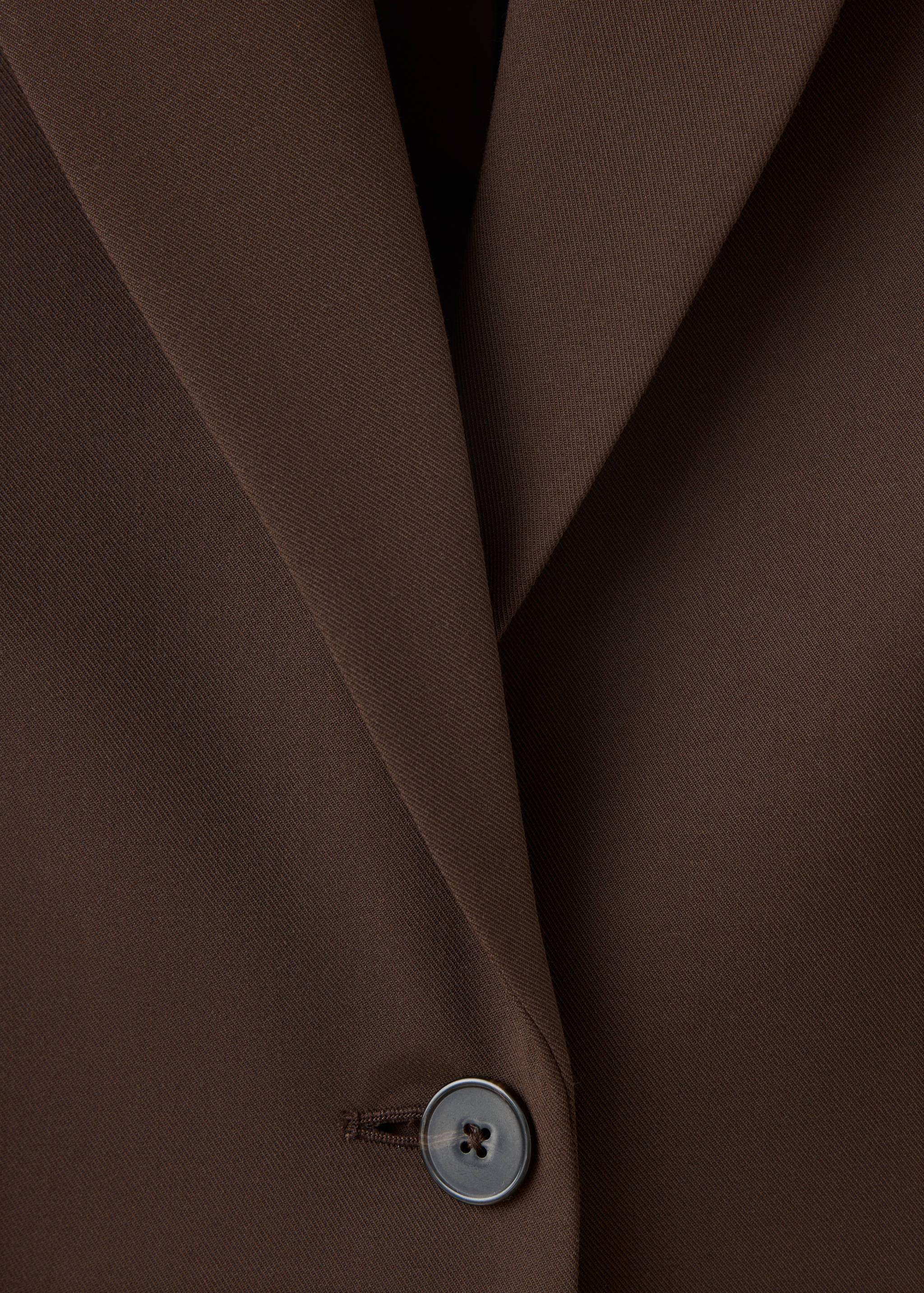 Brown blazer detail showing lapel and button closure.