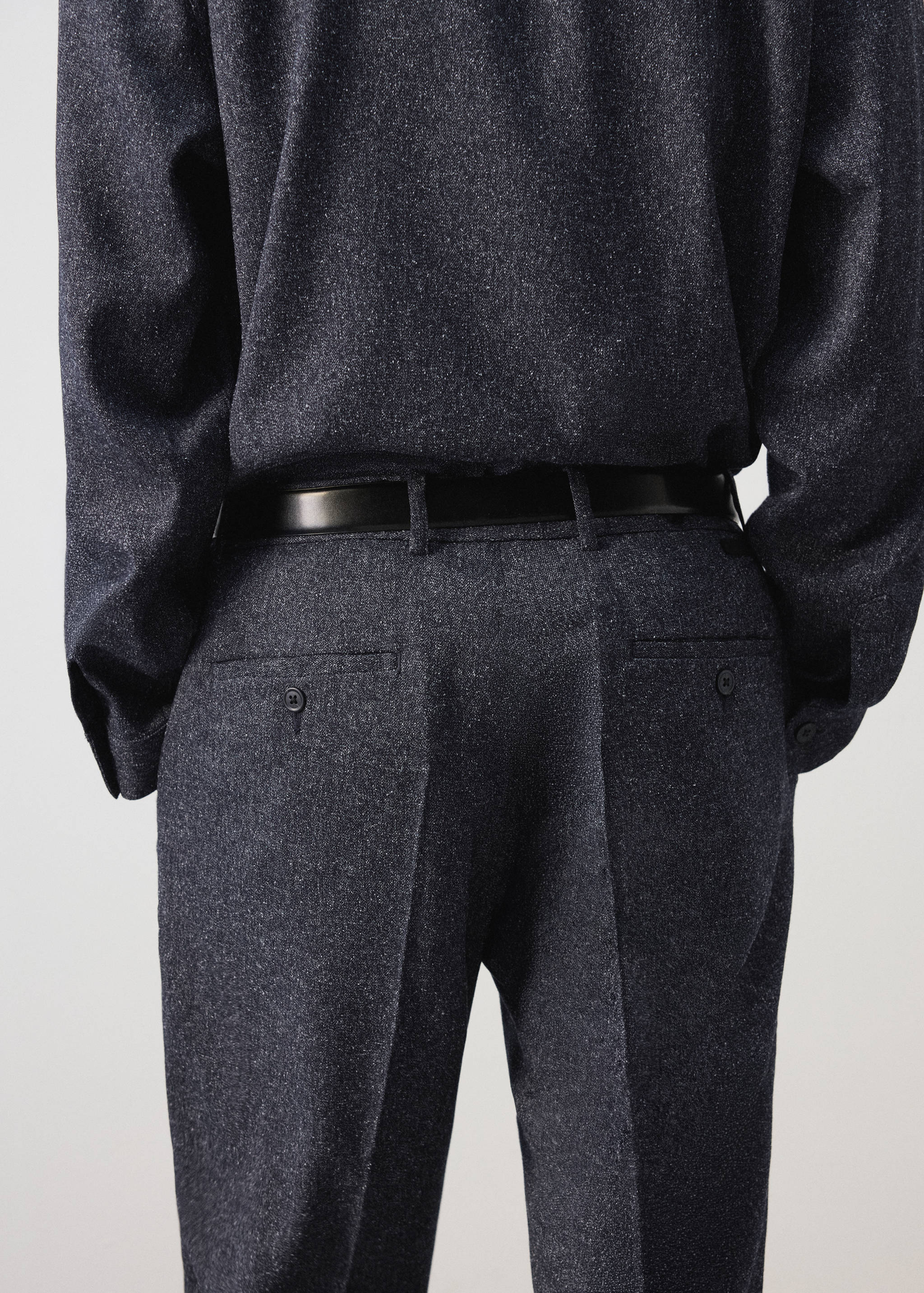 Dark grey speckled trousers with back welt pockets and a black belt.
