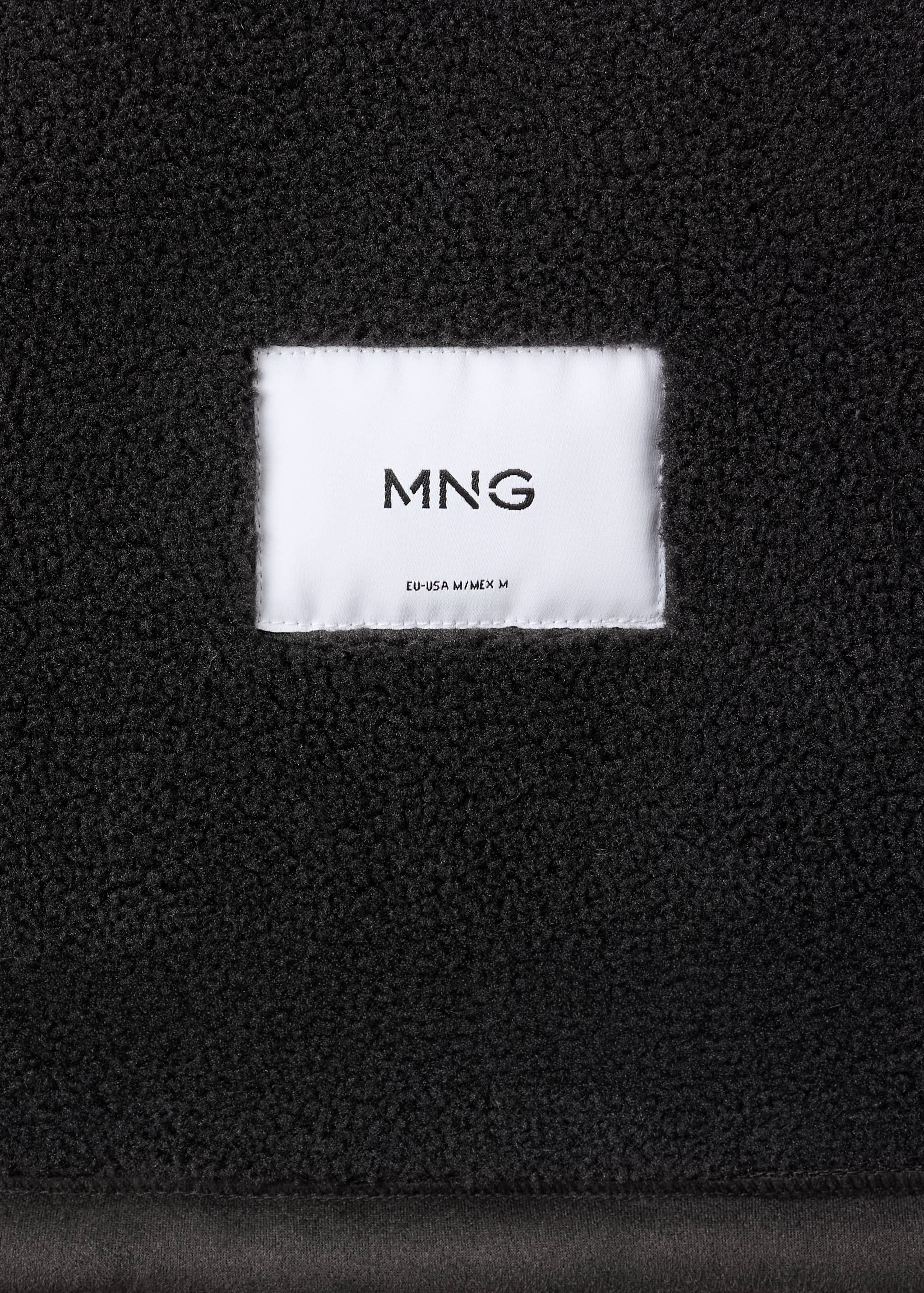 Close-up of black jacket faux-shearling fabric with brand label.