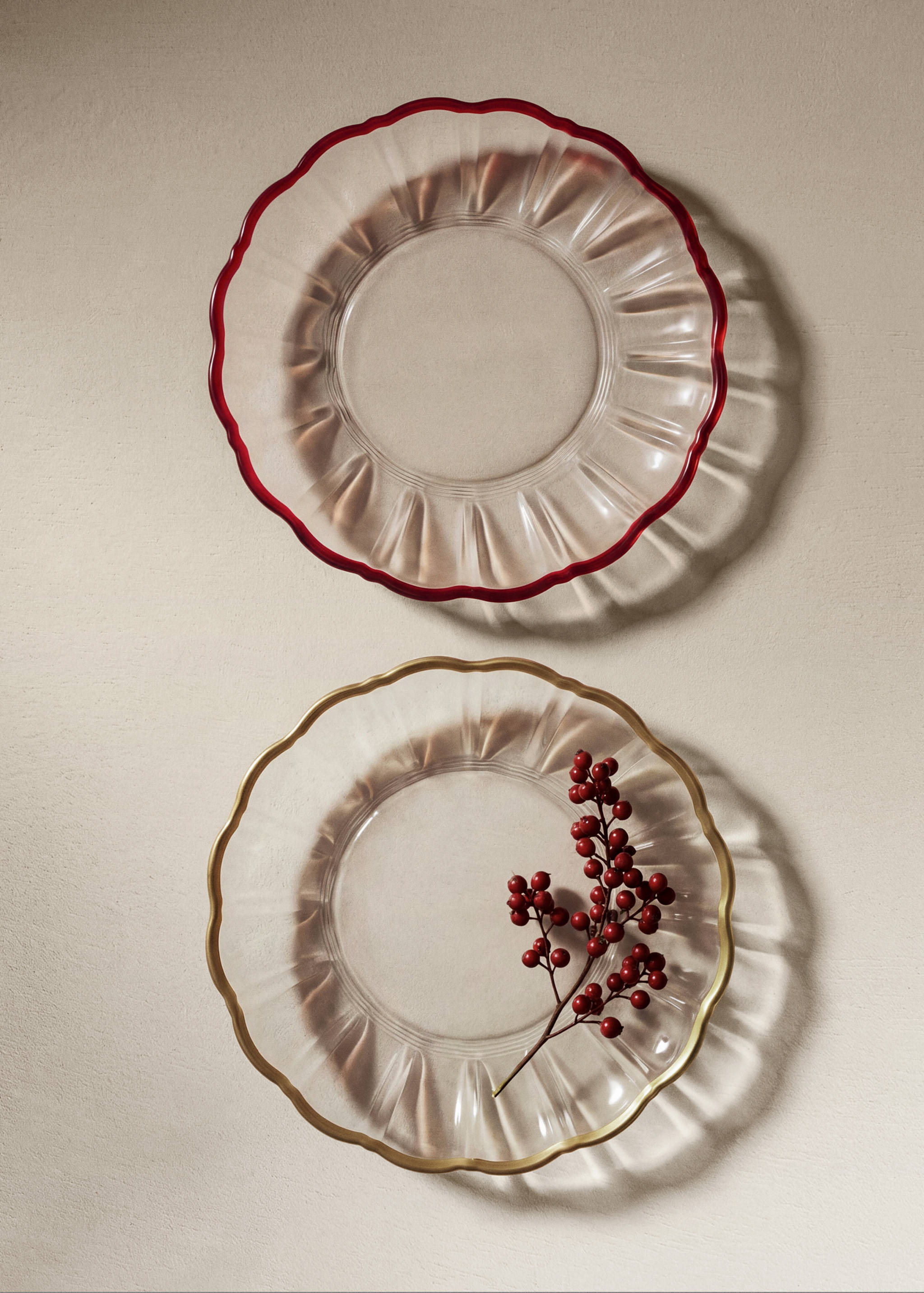 Two round glass plates with scalloped rims, one with a red edge and one with a gold edge.