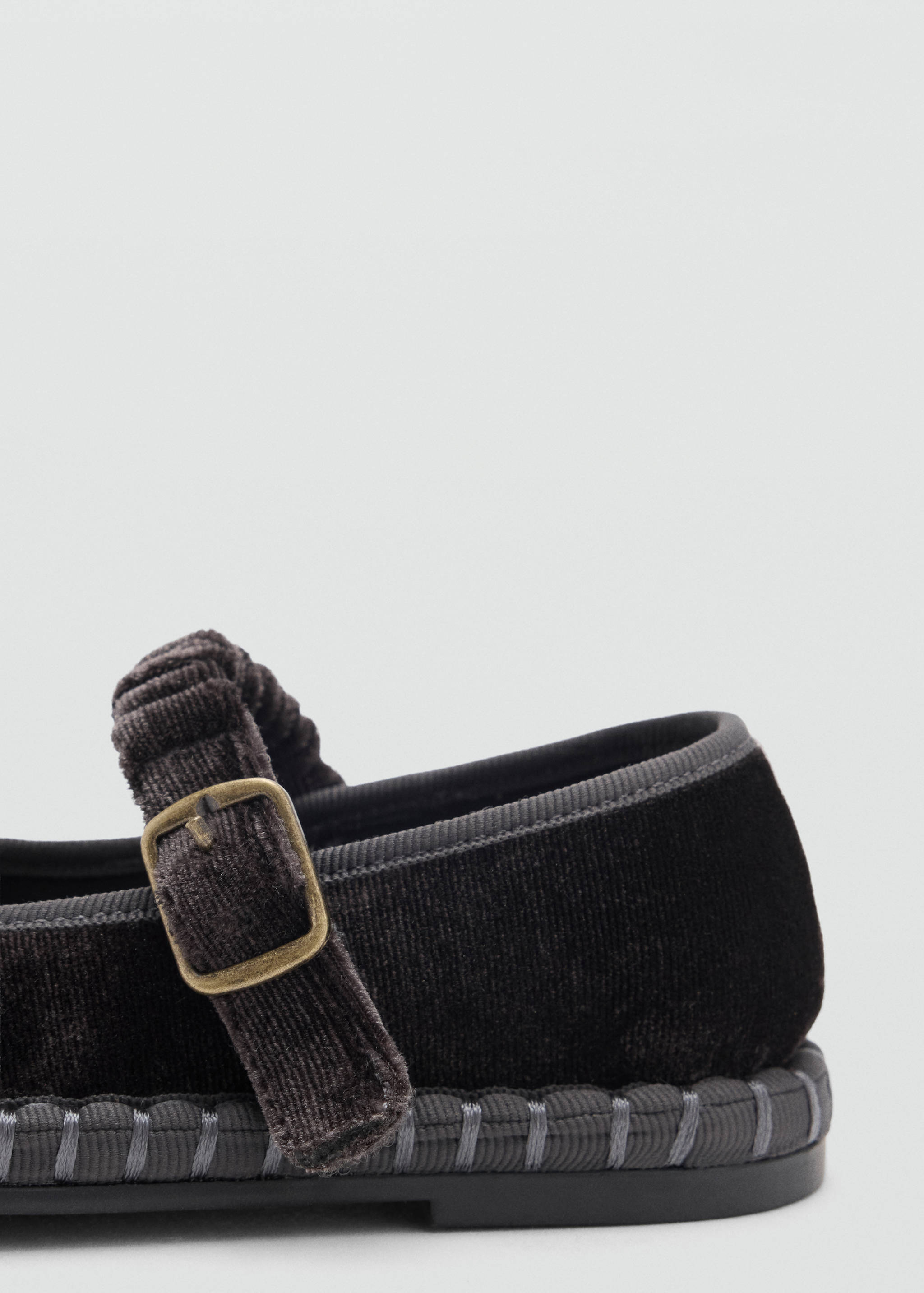 Close-up of a dark grey velvet shoe with a buckle strap and stitched trim.