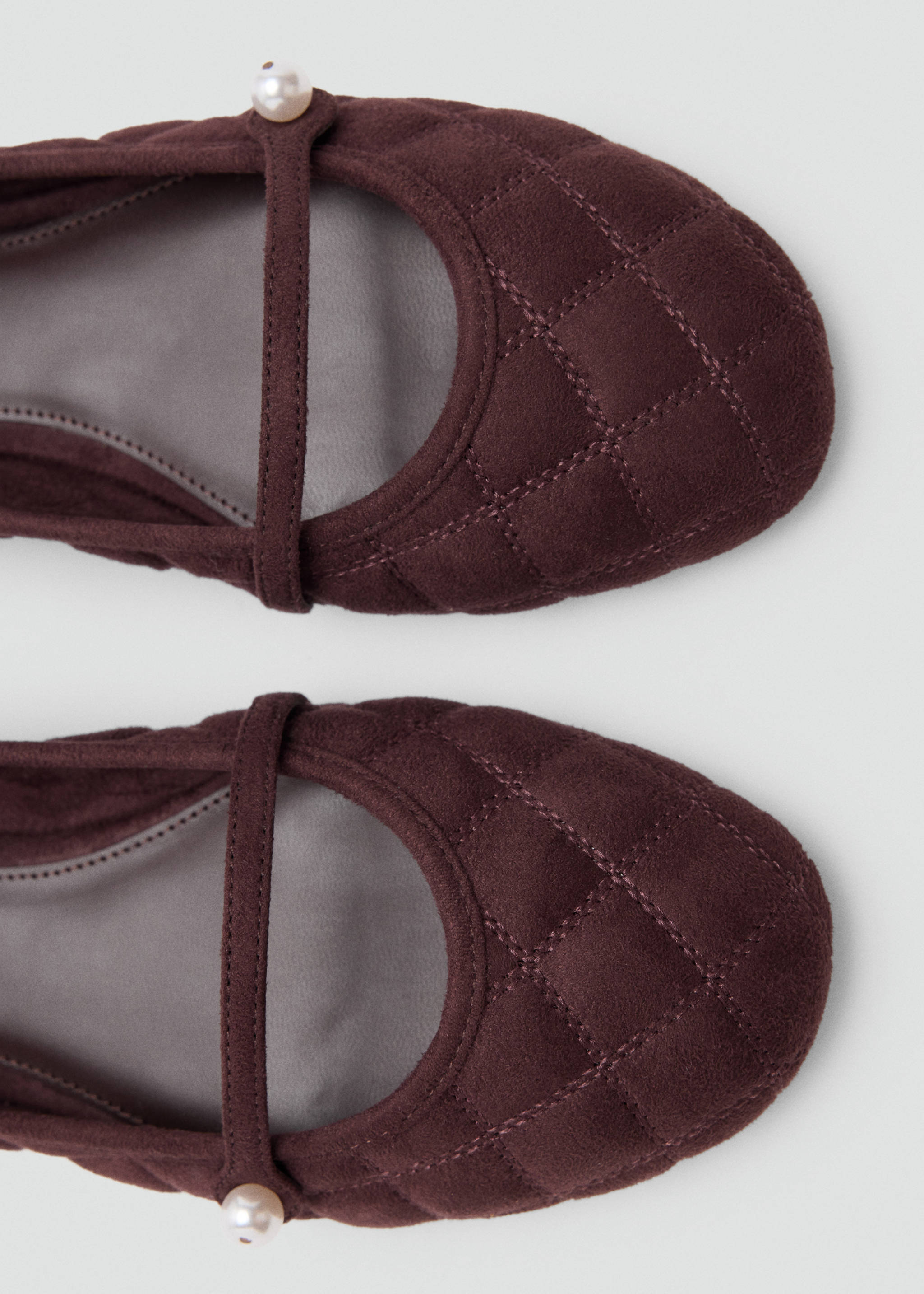 Close-up of burgundy quilted ballet flats with a thin instep strap and pearl detail.
