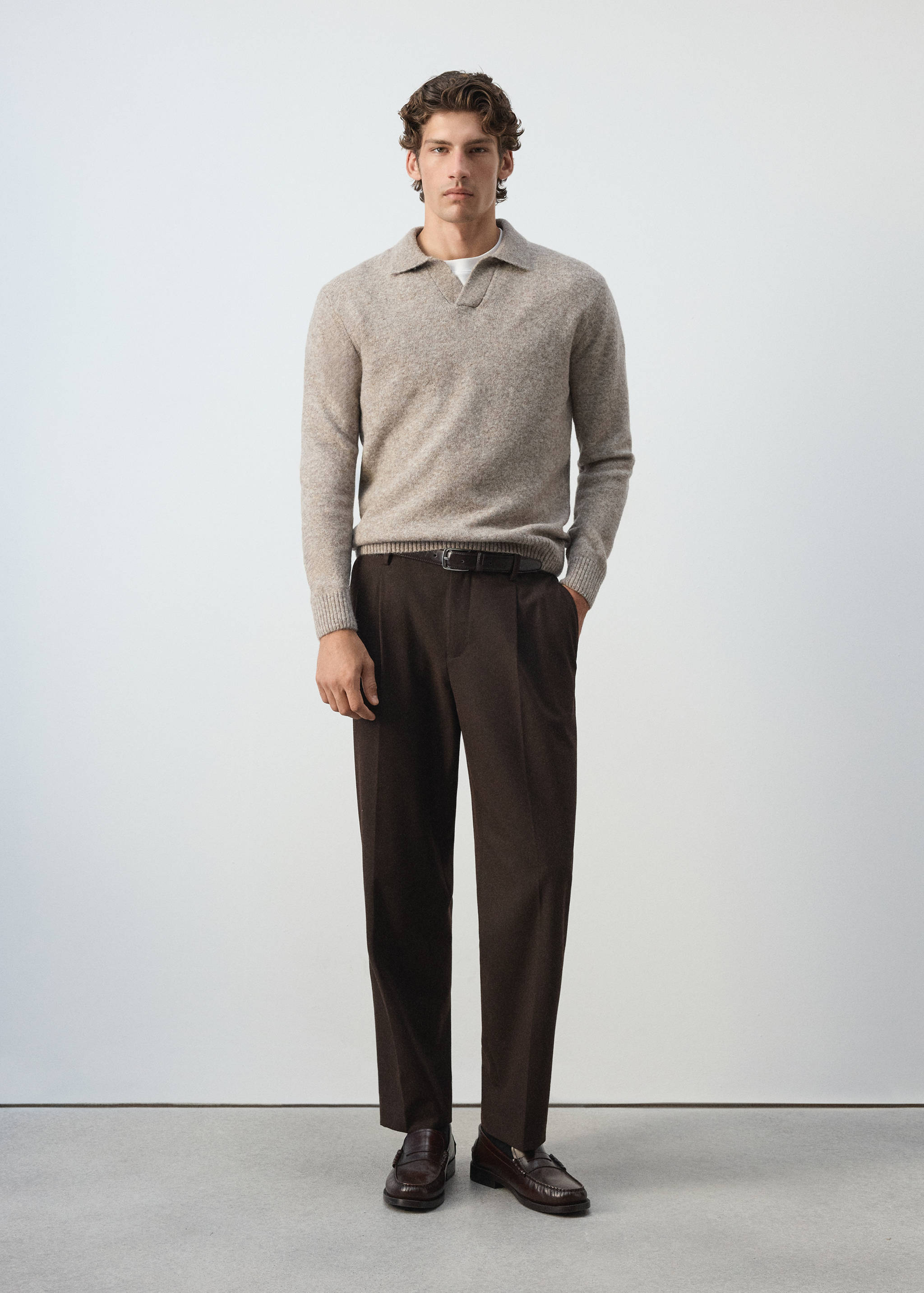 Beige knitted V-neck polo sweater worn with dark brown trousers.