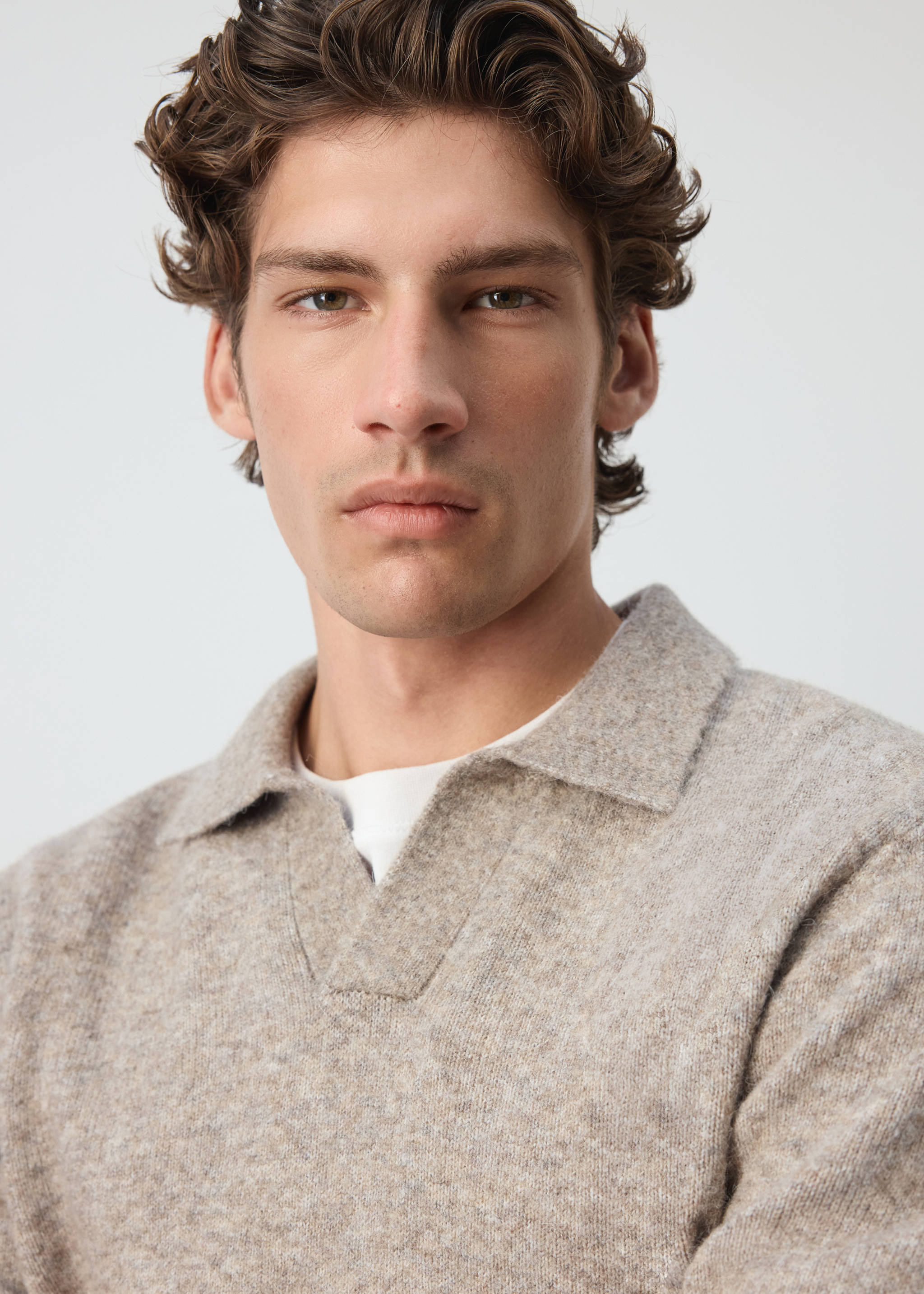 Close-up of a textured beige marled knit polo shirt with a V-neckline.