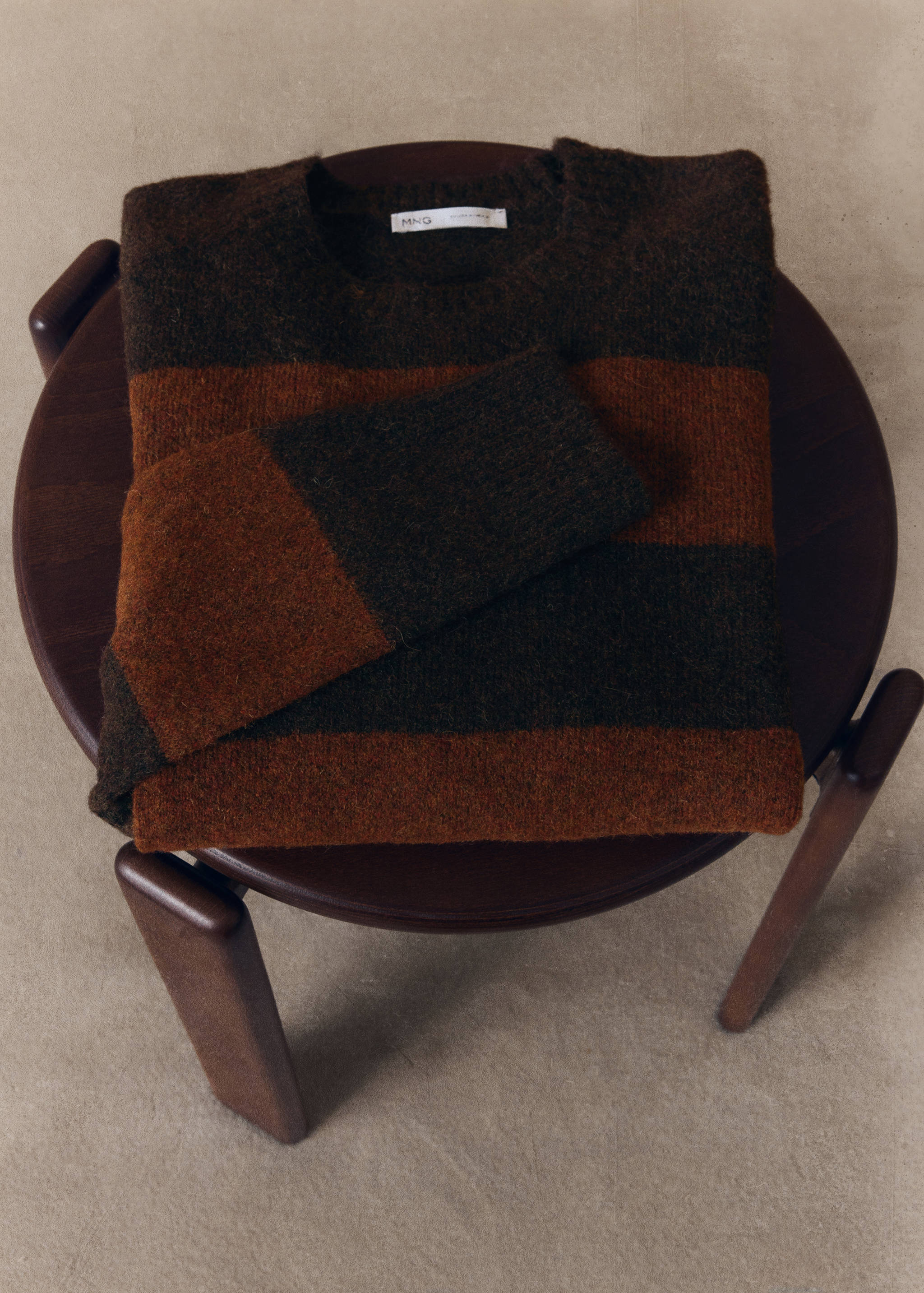 Brown and rust orange striped crew neck sweater in a textured knit, folded on a wooden stool.