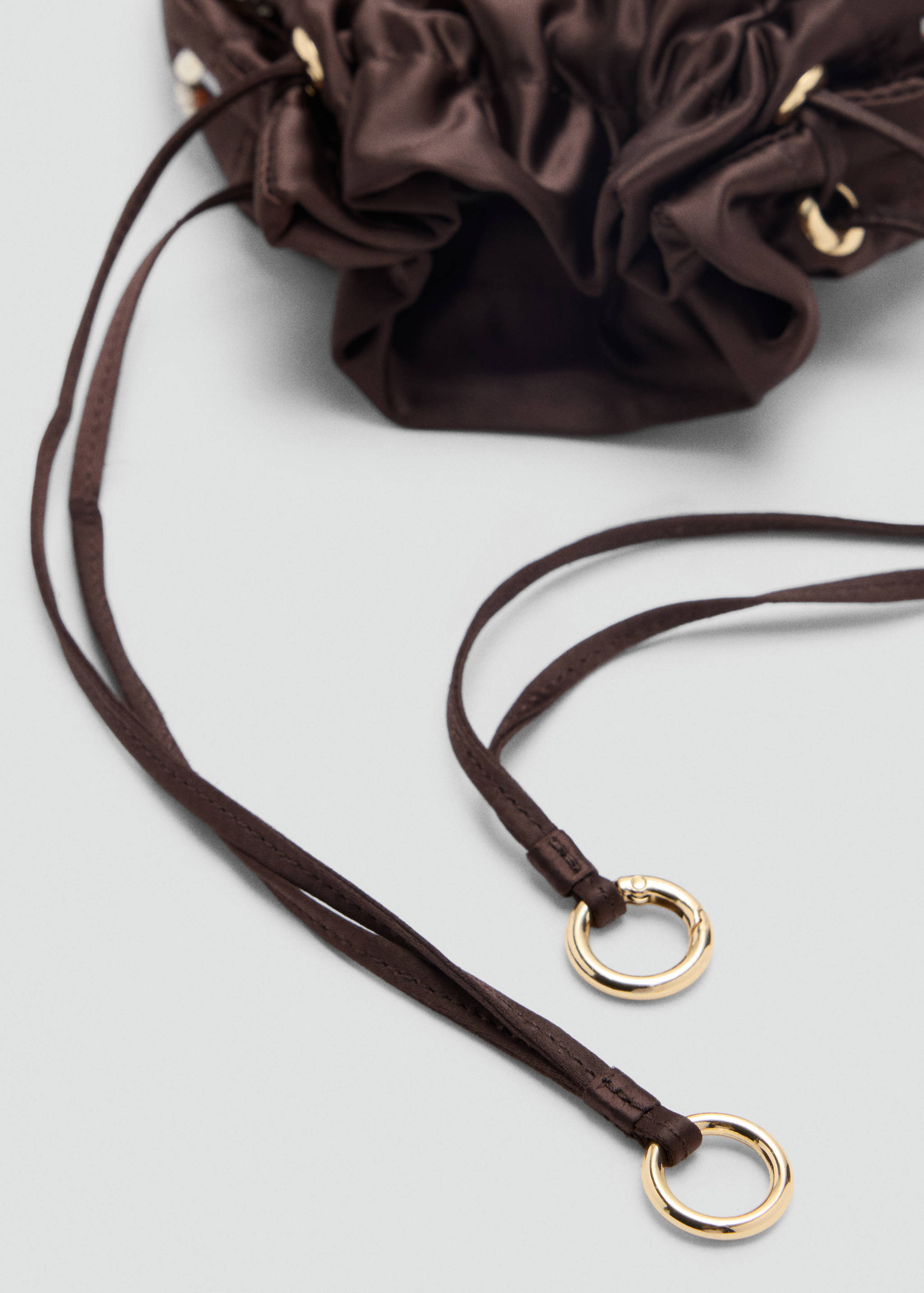 Dark brown satin handbag close-up with gold-toned eyelets and drawstring rings.