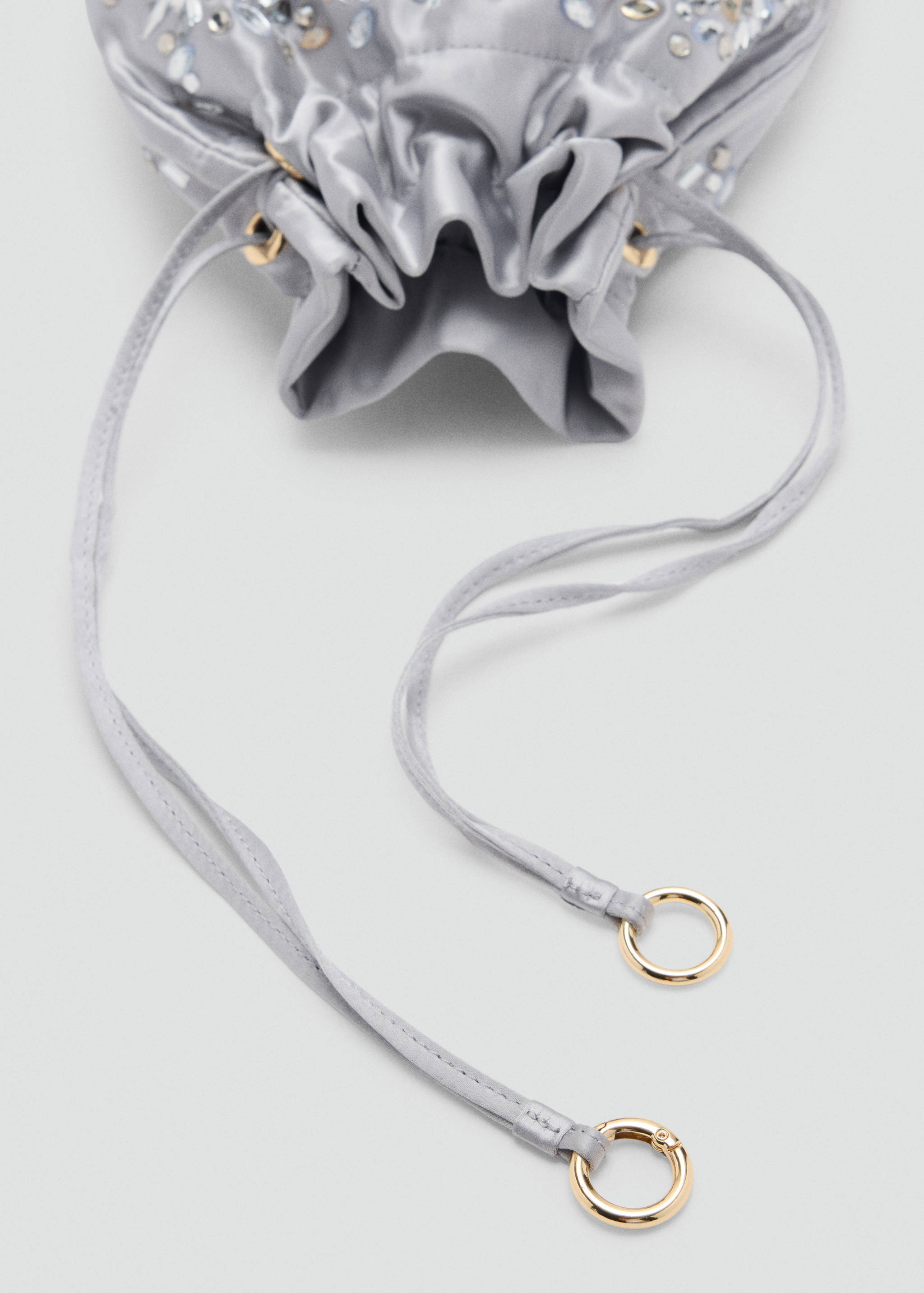 Close-up of a grey satin handbag with a drawstring closure and rhinestone embellishments.