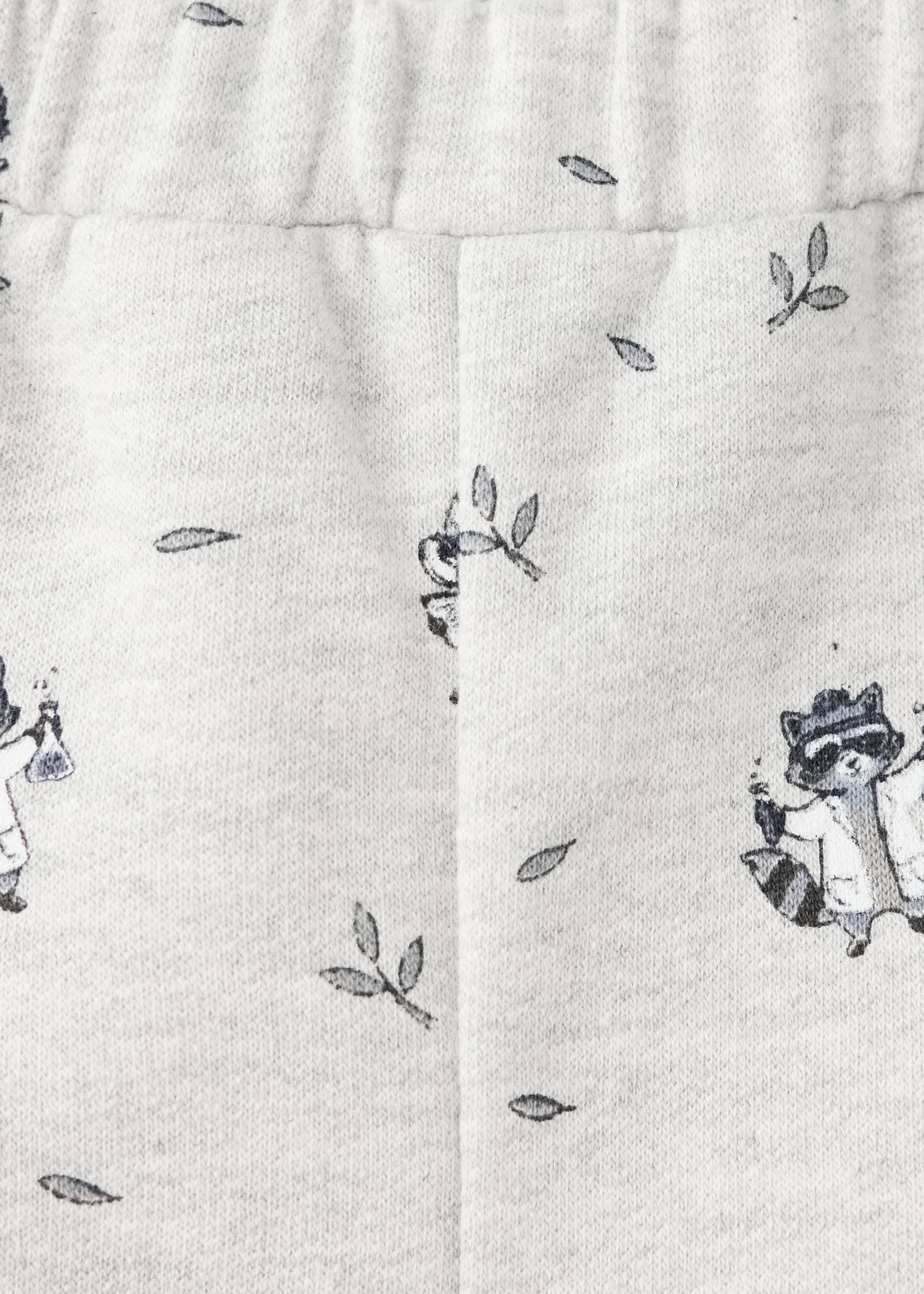 Close-up of joggers with a raccoon and leaf print on light grey marl fabric.
