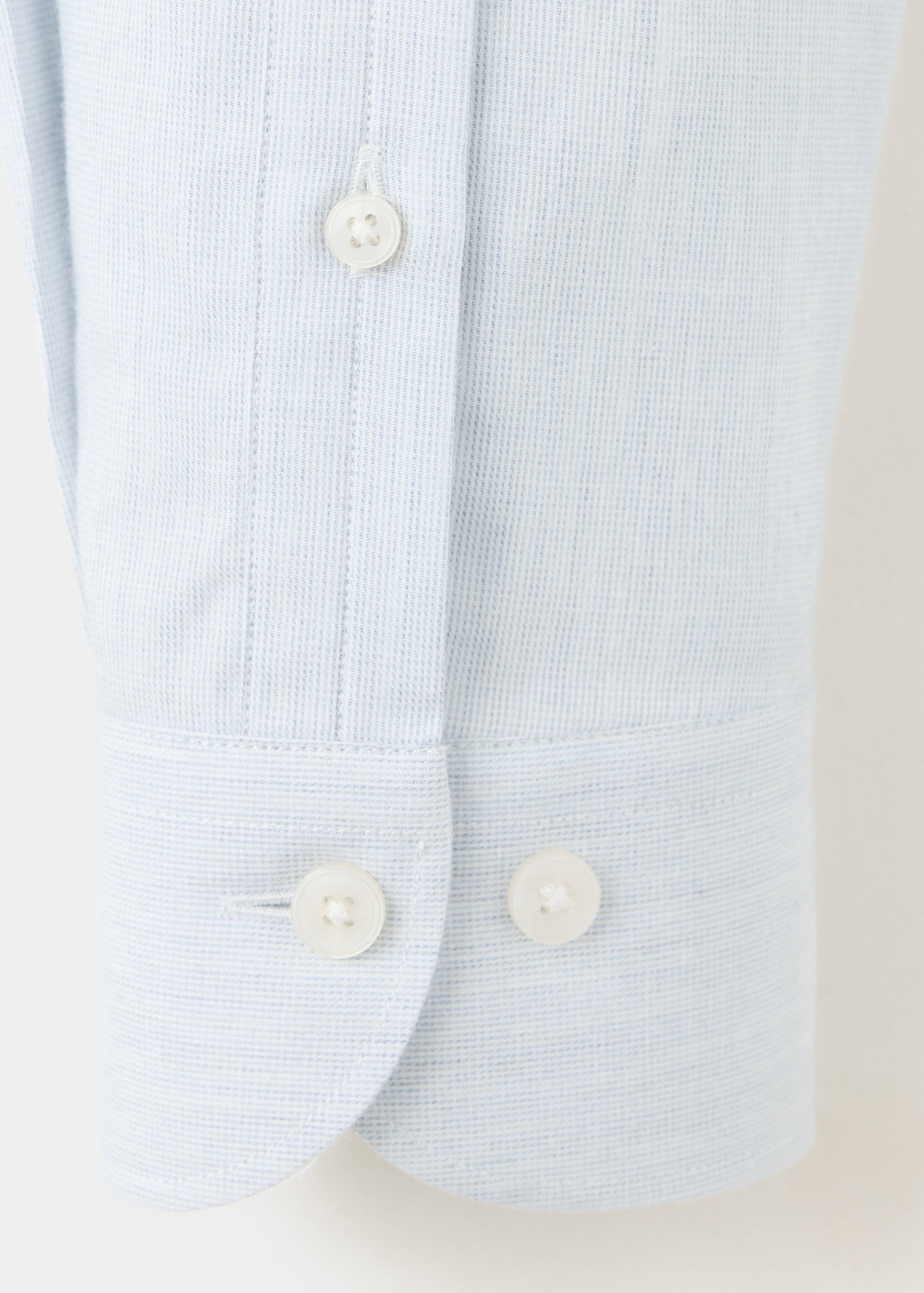 Close-up of a light blue textured shirt cuff and placket with white buttons.