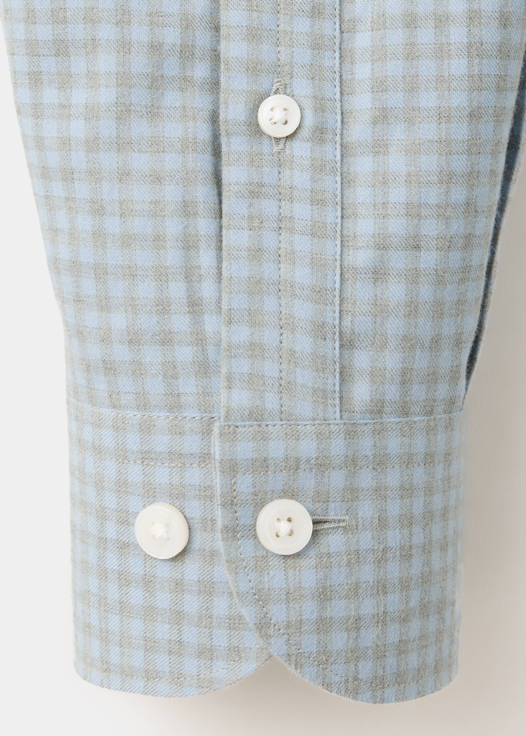 Close-up of a light blue and grey checkered shirt sleeve showing the fabric texture and buttoned cuff.