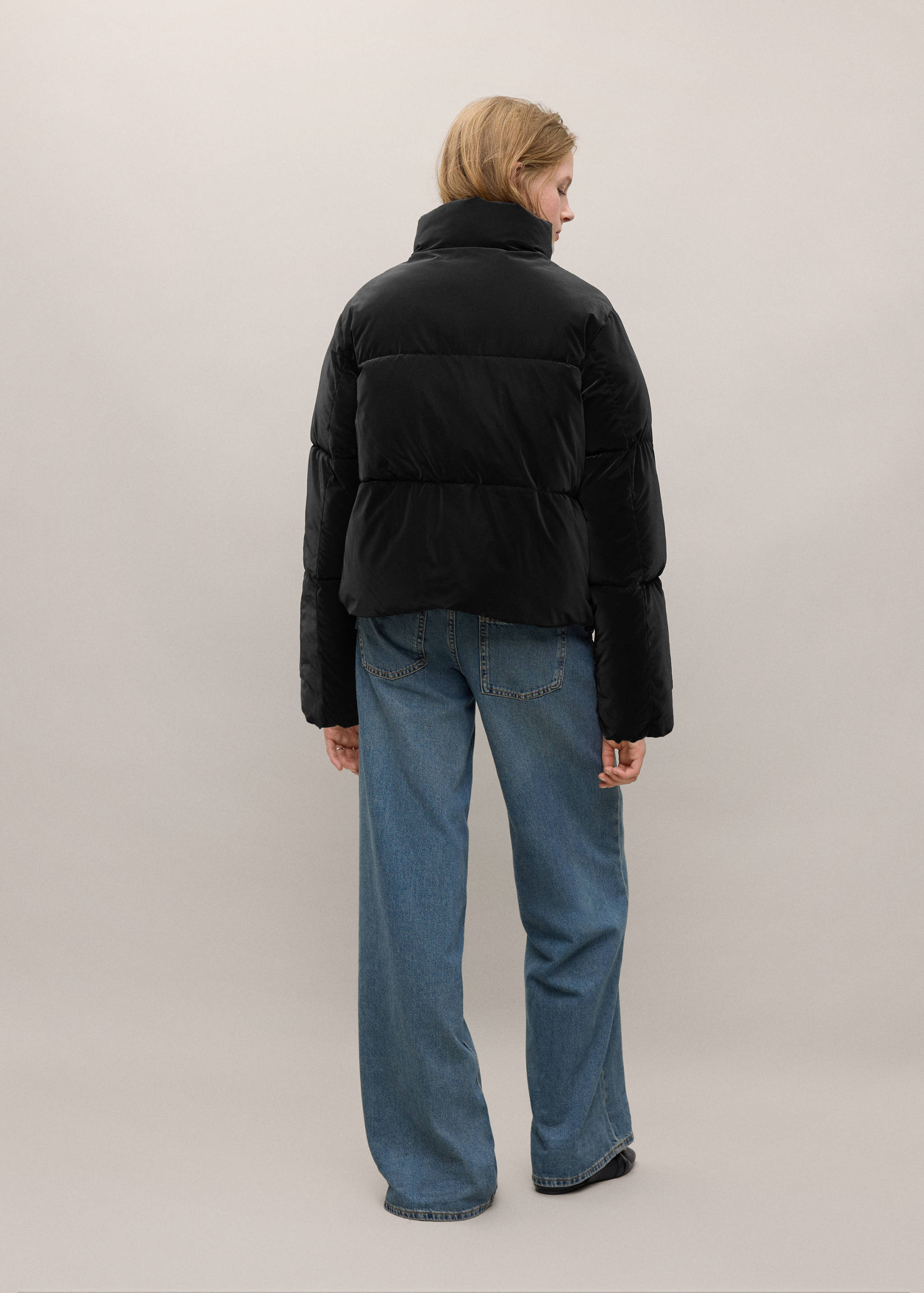 Anorak acolchado negro visto desde atrás, combinado con unos pantalones vaqueros azules.