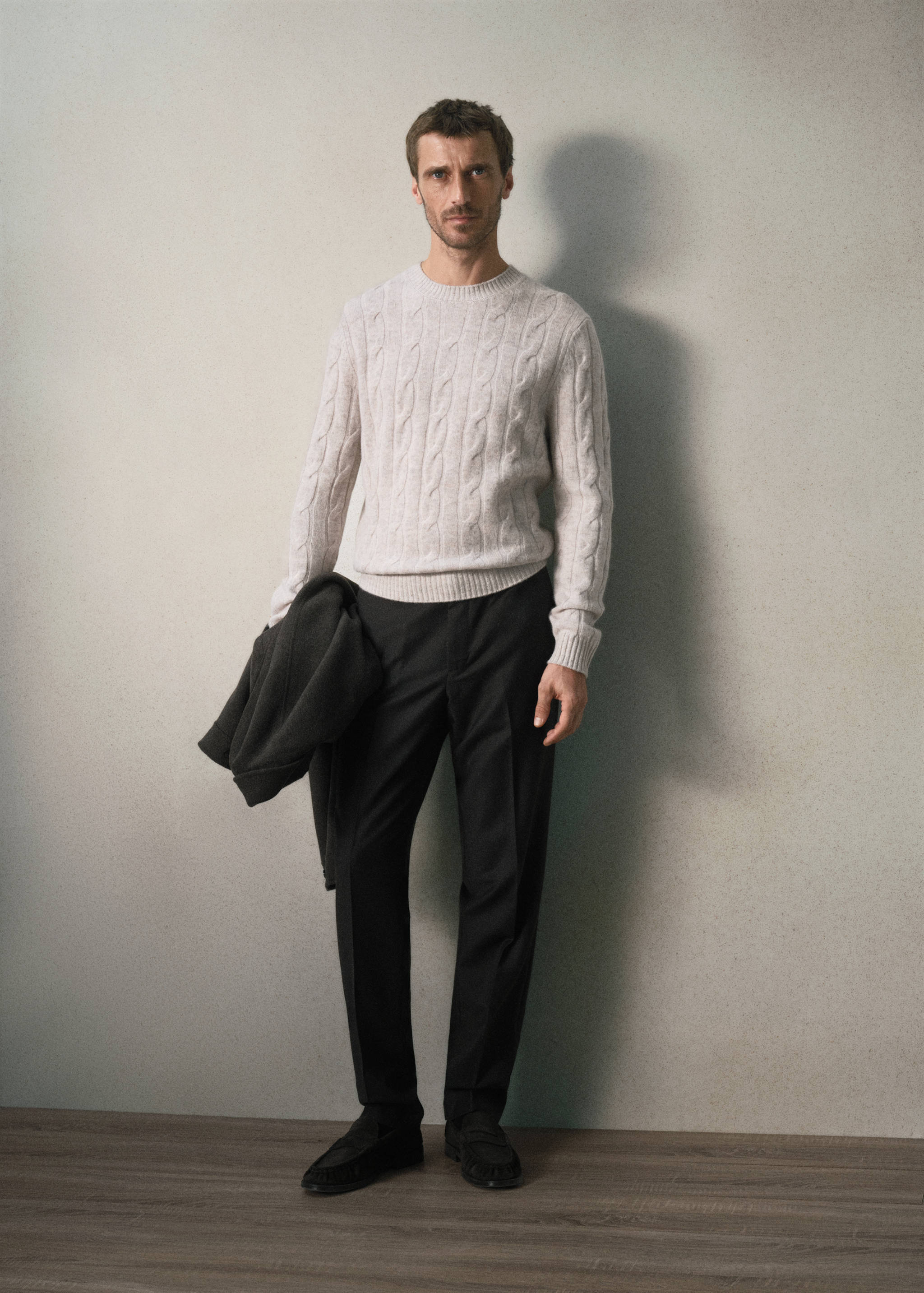 Light grey cable-knit crew neck jersey worn with dark trousers.
